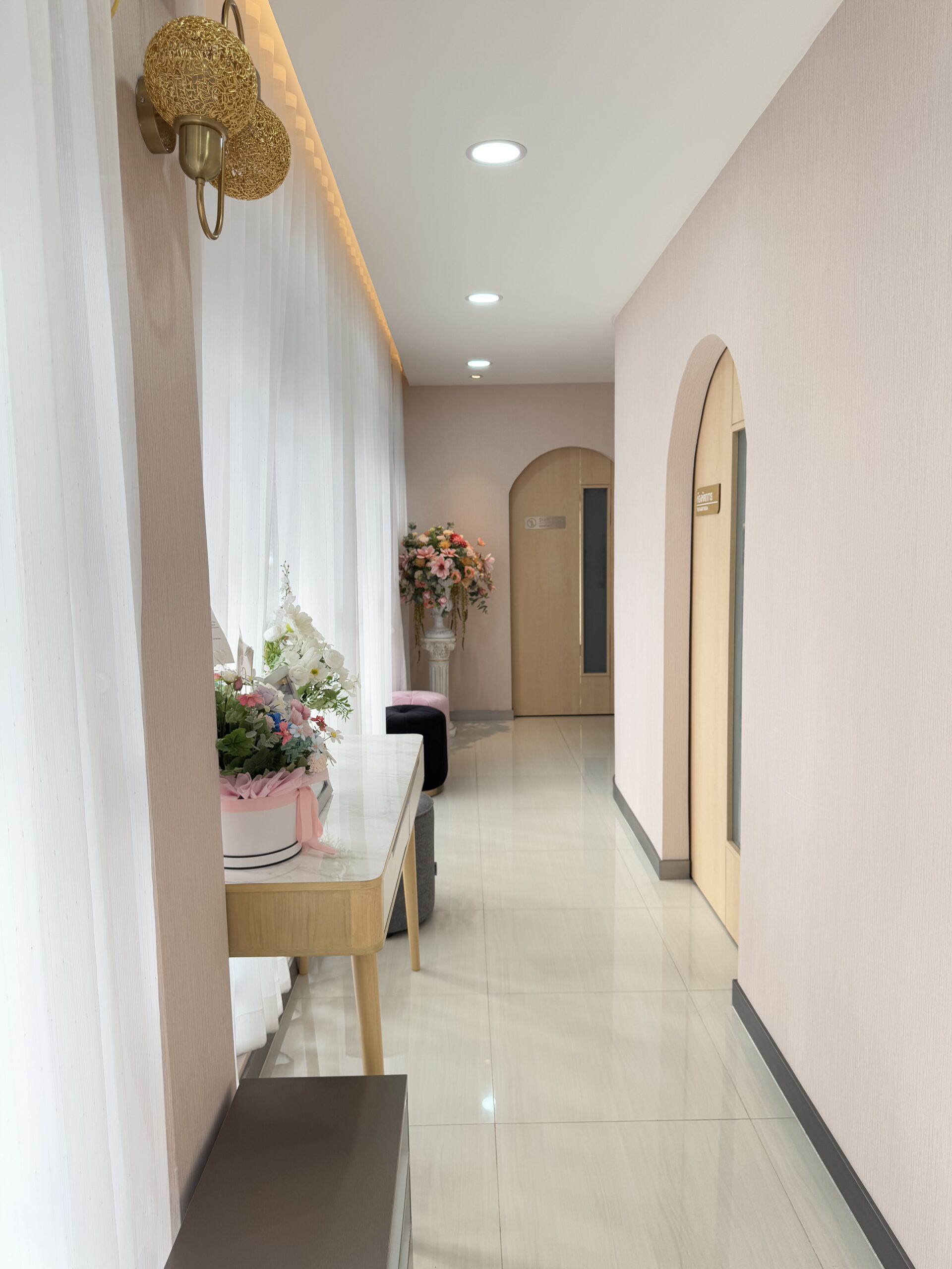 ทางเดินภายในร้านอาหารตกแต่งสวยงามด้วยประตูโค้ง ช่อดอกไม้ ผ้าม่านสีขาว และโคมไฟทองเหลือง บรรยากาศหรูหราอบอุ่น