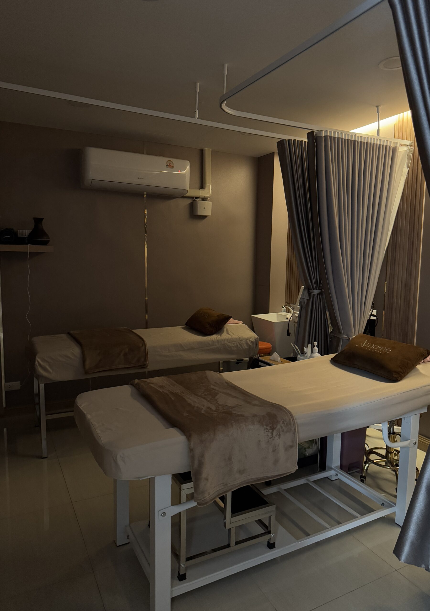 ห้องทรีทเมนต์สปาพร้อมเตียงนวด 2 เตียง ตกแต่งโทนสีน้ำตาลอบอุ่น มีม่านกั้นและเครื่องปรับอากาศ