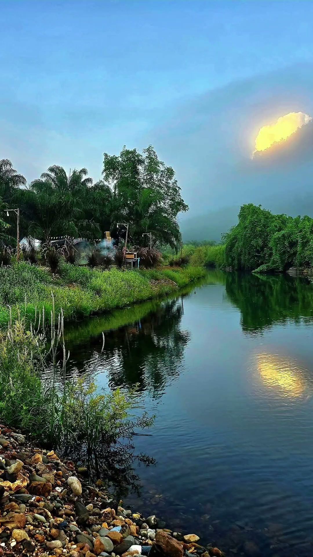 วิวริมแม่น้ำยามเย็นกับต้นไม้เขียวขจีและก้อนหินริมน้ำบรรยากาศร้านอาหารธรรมชาติ