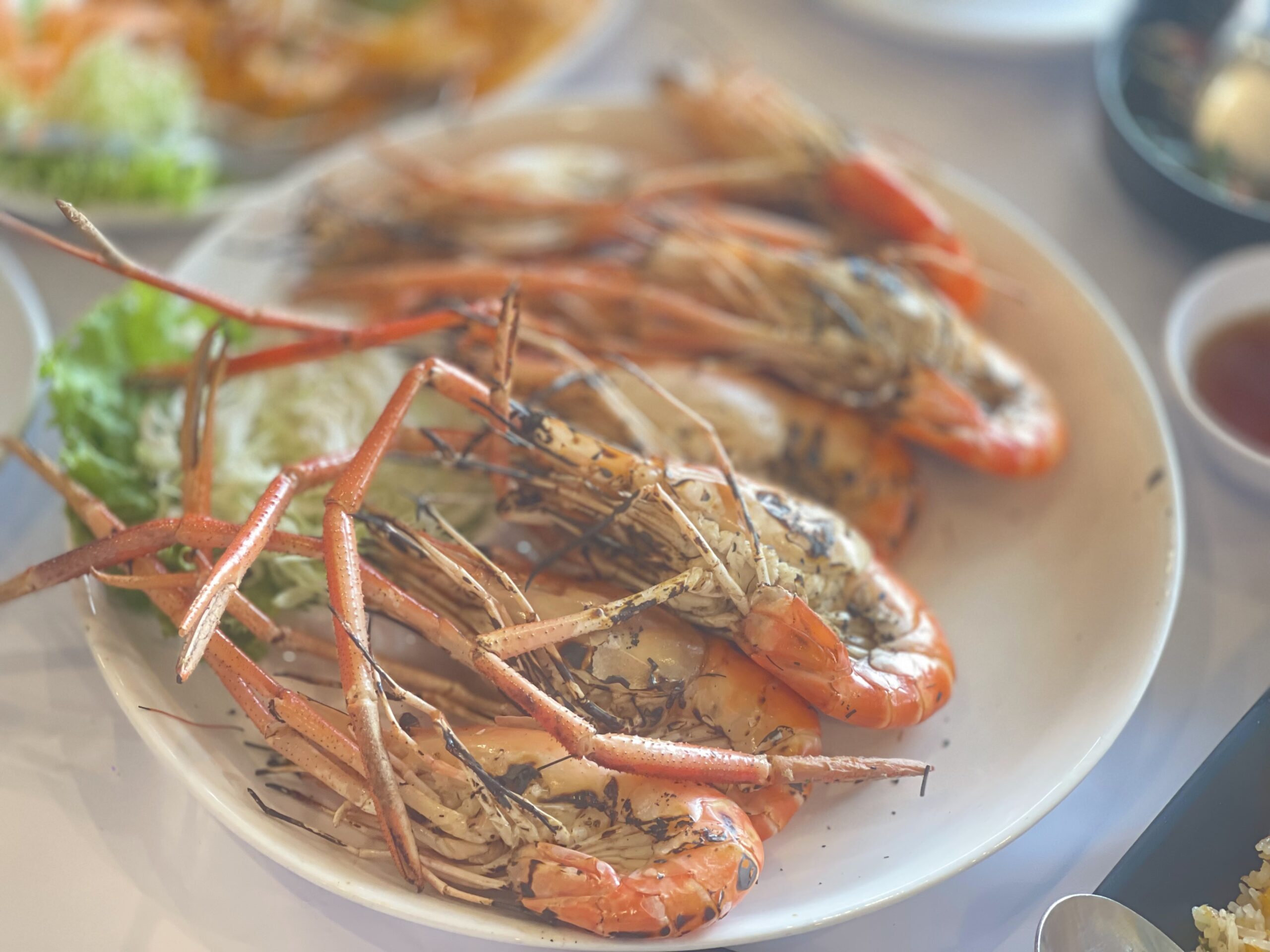 กุ้งแม่น้ำเผาตัวใหญ่เสิร์ฟบนจานขาวพร้อมผักสดและน้ำจิ้มซีฟู้ด