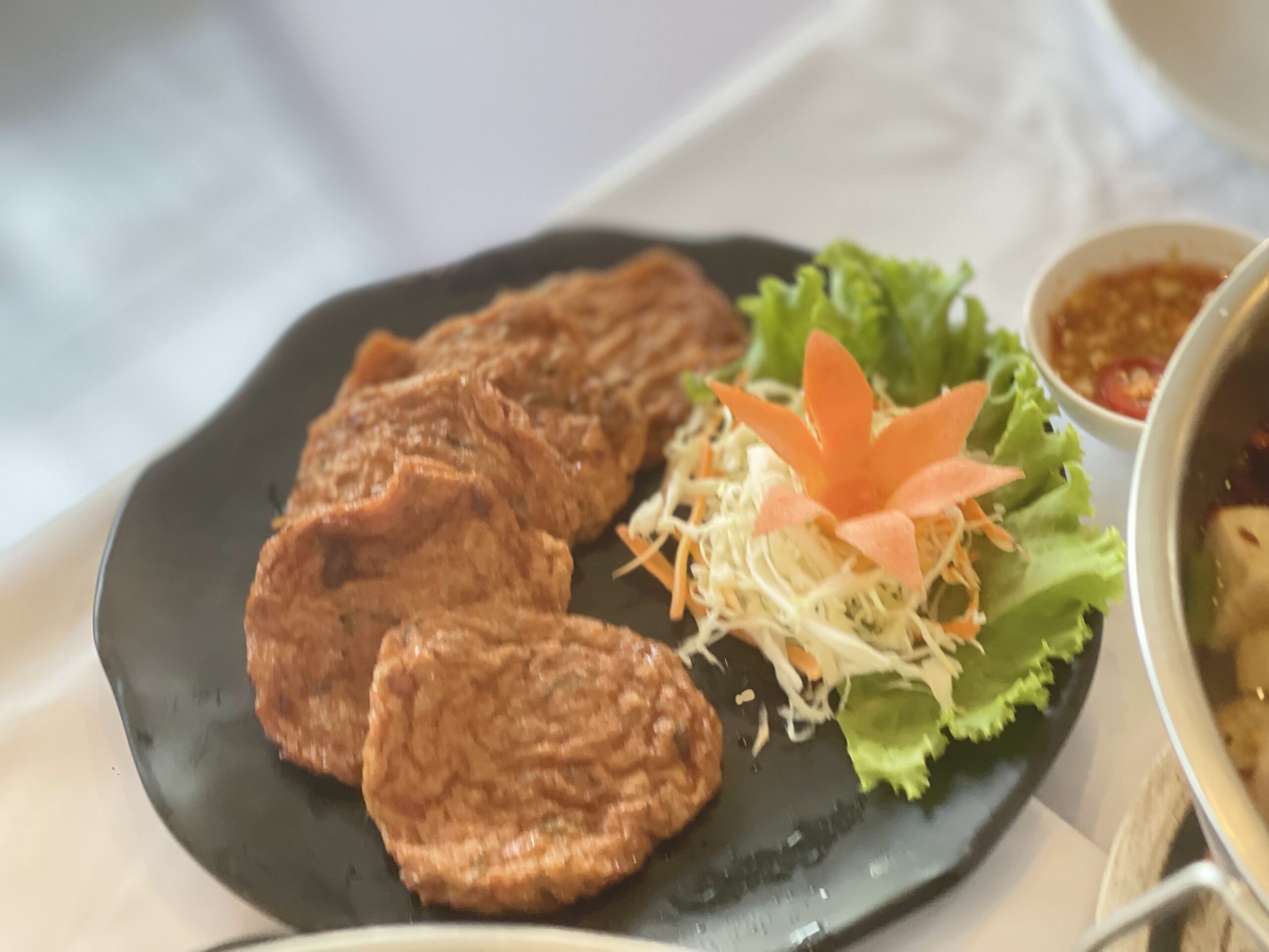 ทอดมันปลาทอดกรอบเสิร์ฟบนจานดำพร้อมผักสลัดและแครอทแกะสลักดอกไม้ คู่กับน้ำจิ้มรสเผ็ด