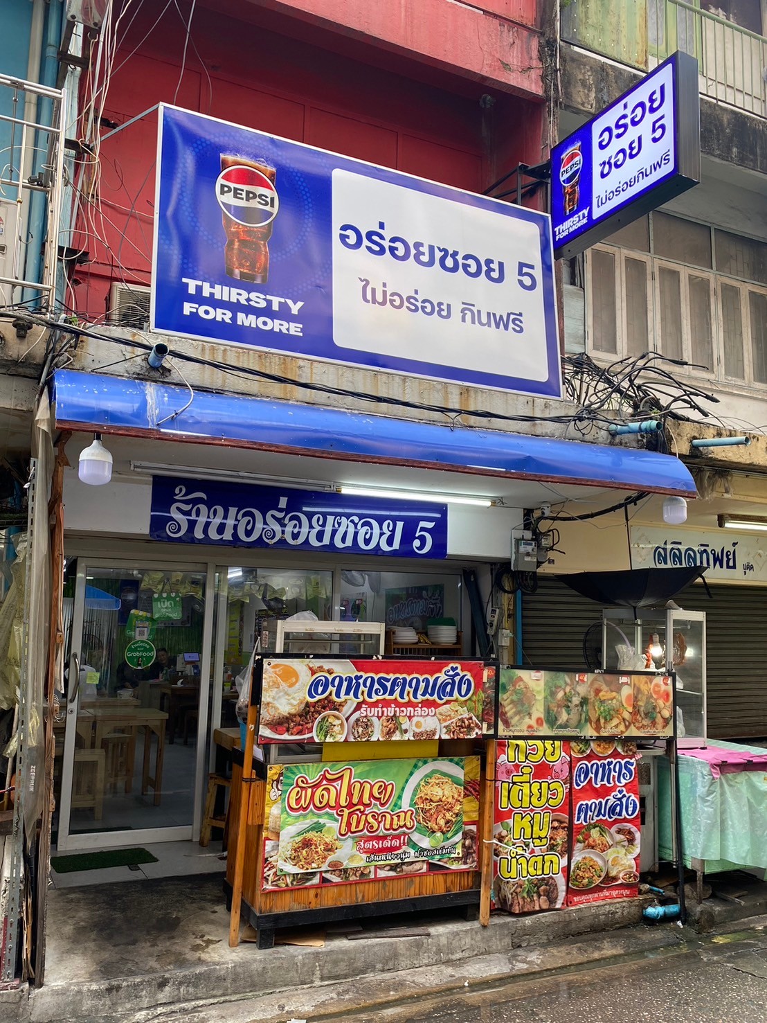 ร้านอร่อยซอย 5 ร้านอาหารตามสั่งริมถนน มีป้ายเปปซี่ขนาดใหญ่ ขายผัดไทยโบราณ ก๋วยเตี๋ยวหมูน้ำตก และอาหารตามสั่ง พร้อมป้ายไม่อร่อยกินฟรี