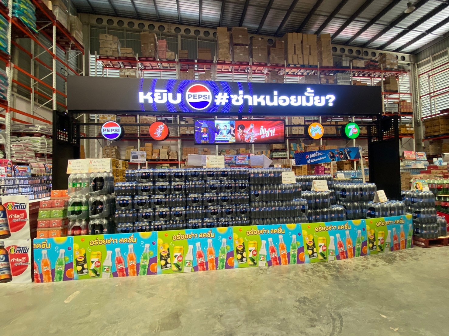 จุดแสดงสินค้าเป๊ปซี่ในโกดังสินค้า มีขวดเป๊ปซี่และ 7Up วางเรียงเป็นชั้นพร้อมป้ายโฆษณา หยิบเป๊ปซี่ ซ่าหน่อยมั้ย