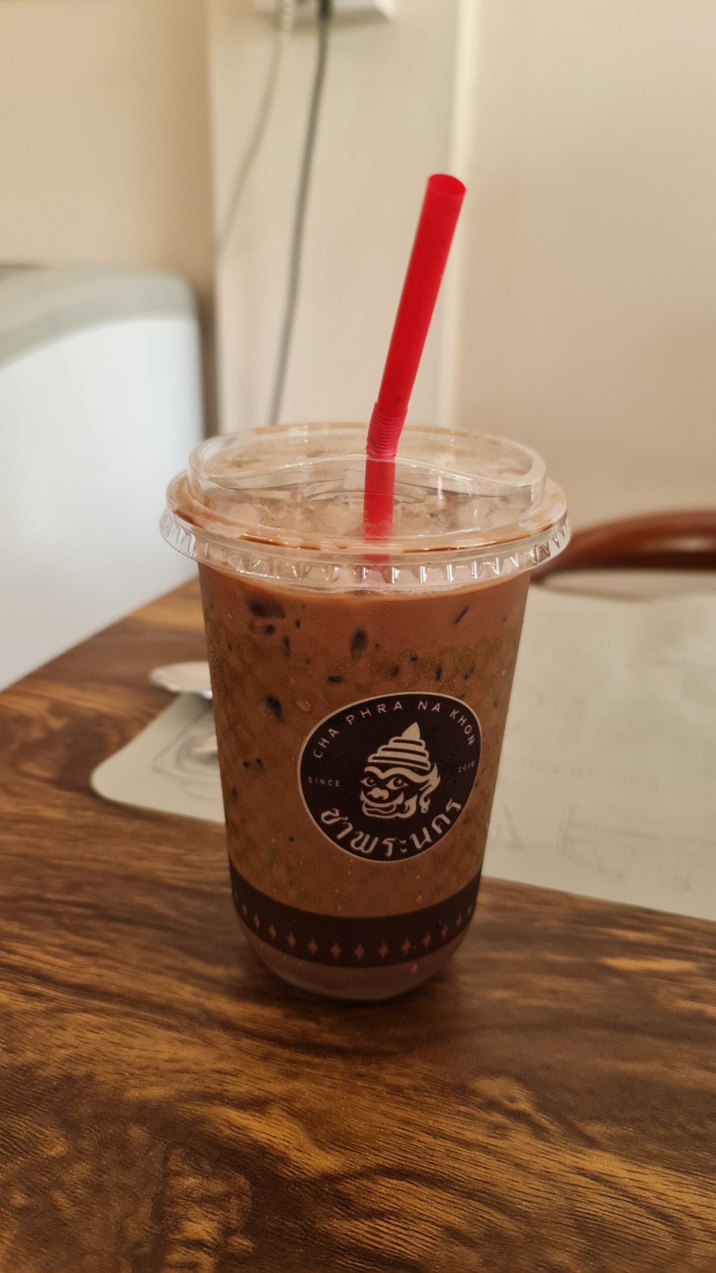 เครื่องดื่มช็อกโกแลตเย็นในแก้วพลาสติกจากร้านชาพระนคร พร้อมหลอดสีแดง วางบนโต๊ะไม้