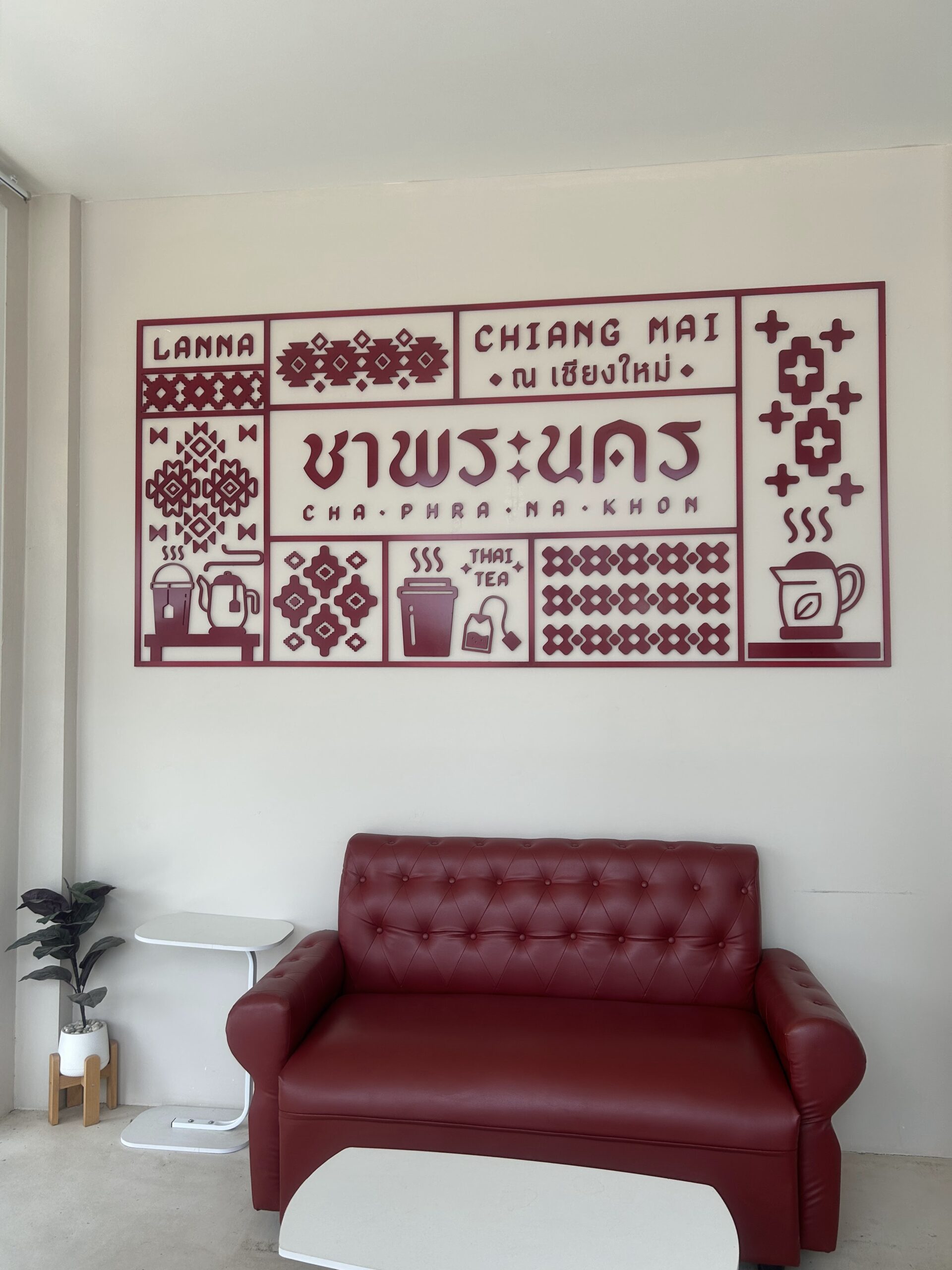 ป้ายตกแต่งผนังร้านชาพระนคร เชียงใหม่ สไตล์ล้านนา สีแดงเลือดหมูบนผนังขาว พร้อมโซฟาหนังสีแดงเข้ม
