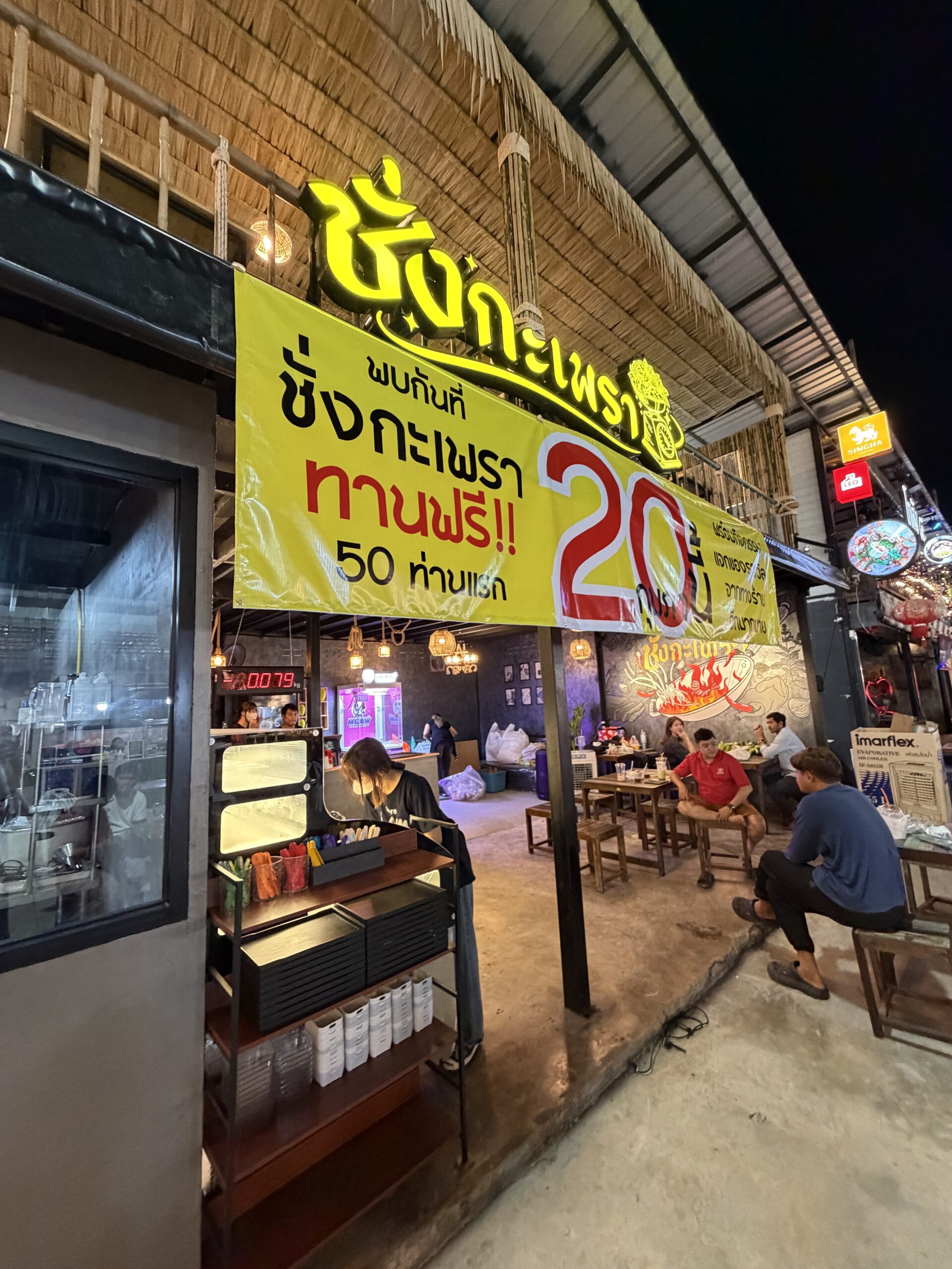 ร้านชิ้งกะเพรา ป้ายโปรโมชั่นทานฟรี 50 ท่านแรก บรรยากาศร้านอาหารตอนกลางคืนกับลูกค้านั่งทาน