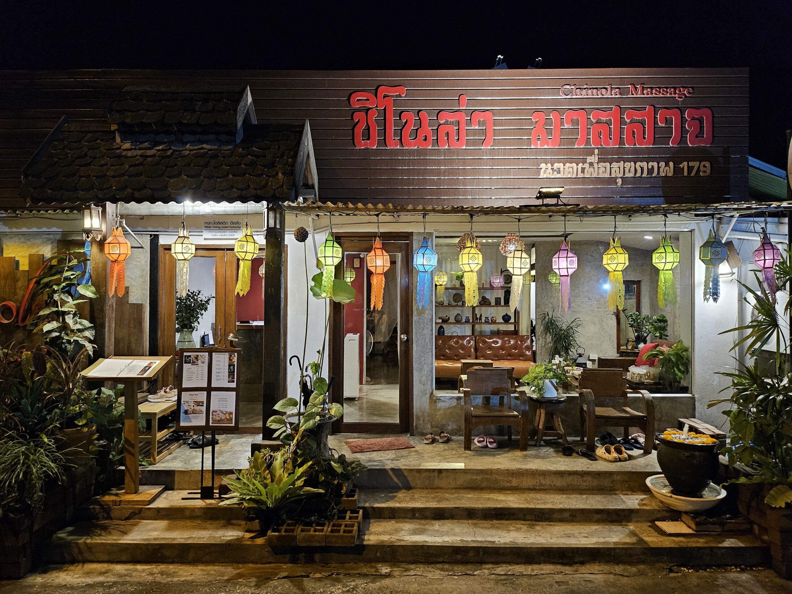 ร้านชิโนล่า มาสสาจ ถ่ายตอนกลางคืน มีโคมไฟล้านนาสีสันสดใสแขวนประดับหน้าร้าน บรรยากาศอบอุ่นน่าเข้า