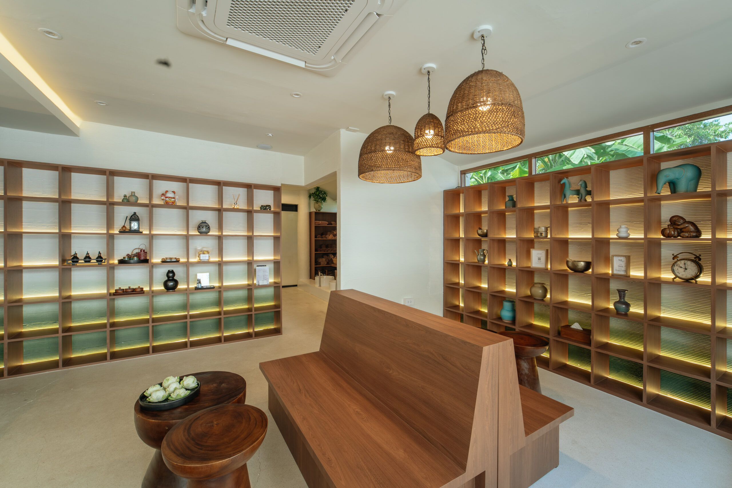 ล็อบบี้ร้านอาหารตกแต่งด้วยชั้นไม้แสดงของสะสม โคมไฟหวายแขวนเพดาน และม้านั่งไม้สไตล์โมเดิร์น