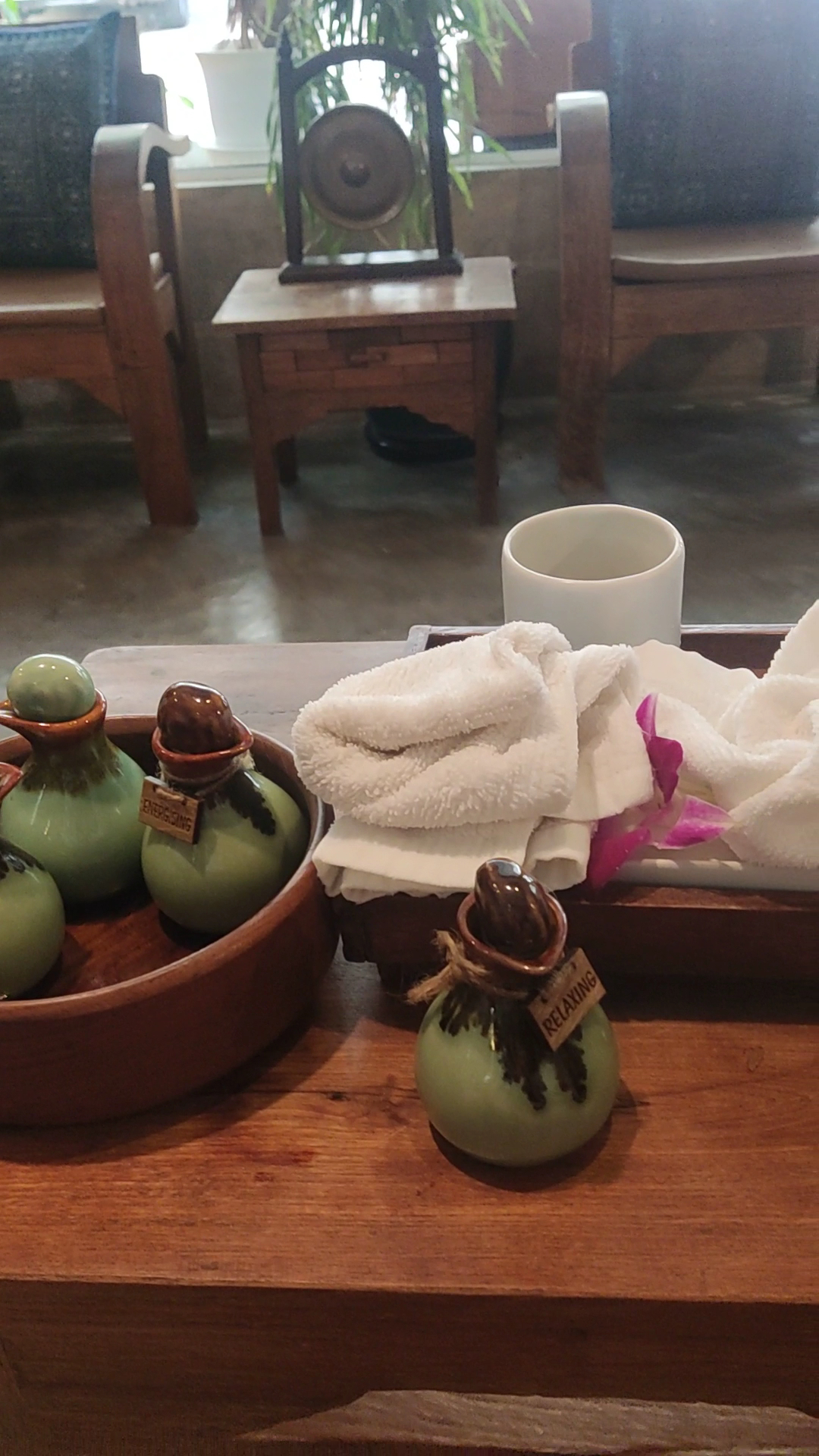 ขวดน้ำมันอโรมาเธอราปีสีเขียวพร้อมผ้าขนหนูสีขาวและดอกกล้วยไม้สีชมพูบนถาดไม้ในสปา