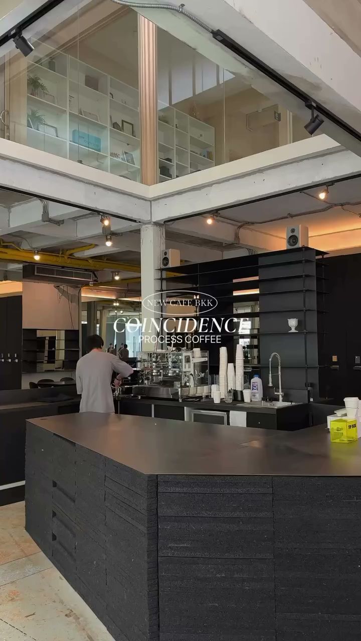 เคาน์เตอร์บาร์สีดำของร้านกาแฟ Coincidence Process Coffee ในกรุงเทพฯ พร้อมเครื่องชงกาแฟและบาริสต้ากำลังทำเครื่องดื่ม ภายในอาคารสไตล์ลอฟท์