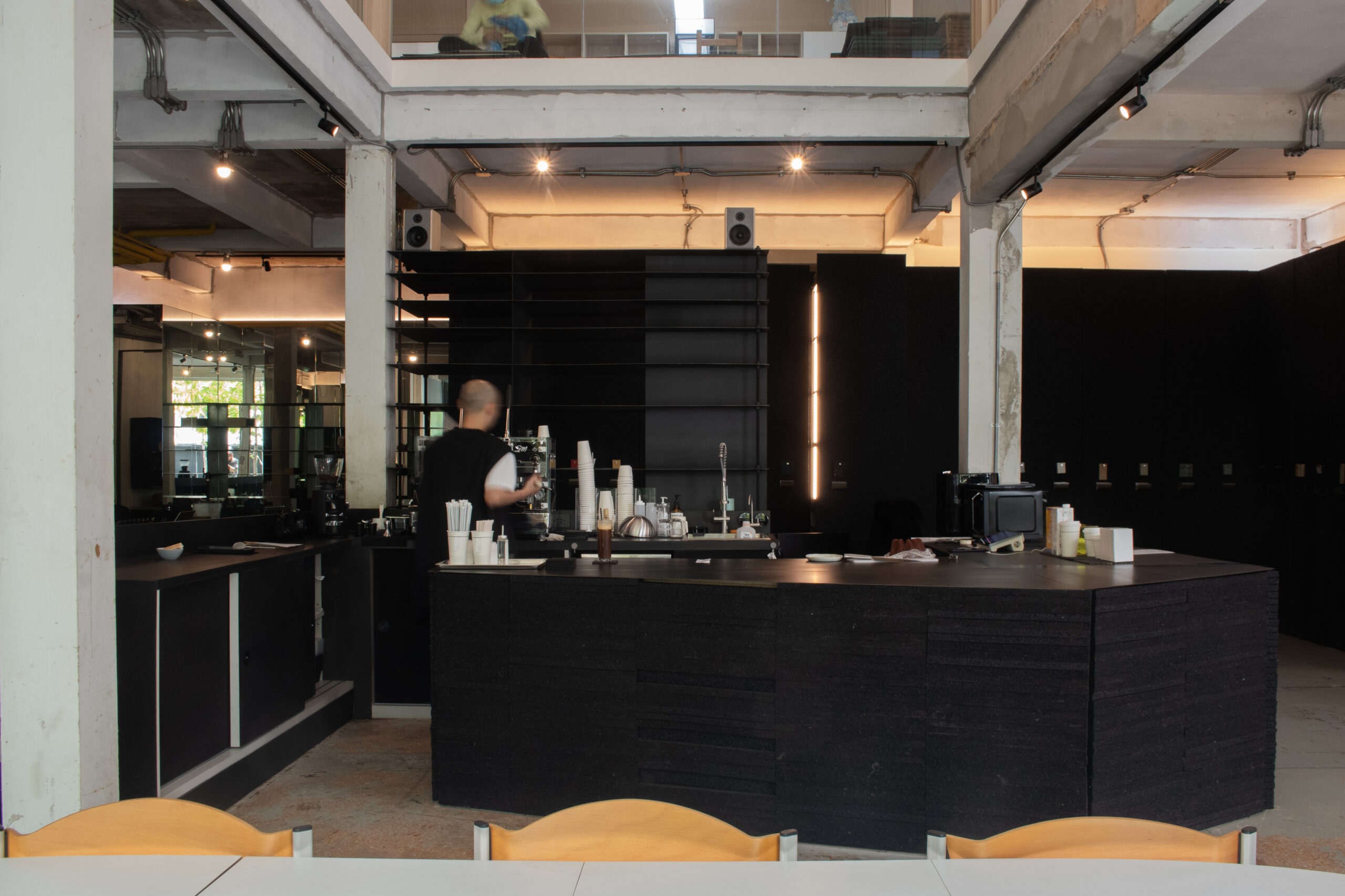 เคาน์เตอร์บาร์กาแฟสีดำในสไตล์อินดัสเทรียลลอฟท์ มีบาริสต้ากำลังชงกาแฟ พร้อมอุปกรณ์และแก้วกาแฟเรียงบนเคาน์เตอร์