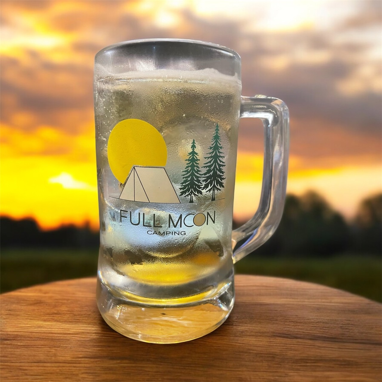แก้วเบียร์ใสมีโลโก้ Full Moon Camping พร้อมรูปเต็นท์และต้นสนบนพื้นหลังพระอาทิตย์ตก