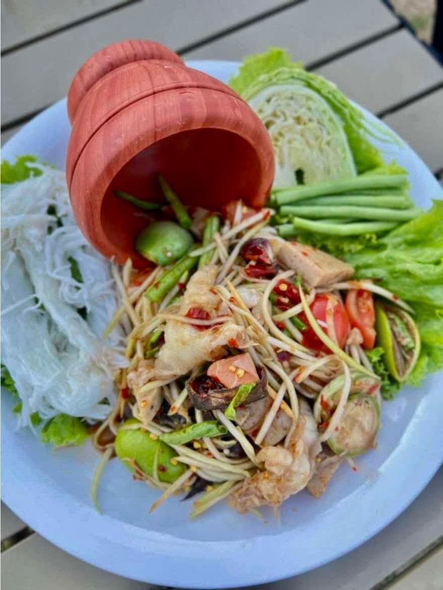 ส้มตำไทยเสิร์ฟพร้อมขนมจีน ผักสด และครกดินเผา บนจานขาว
