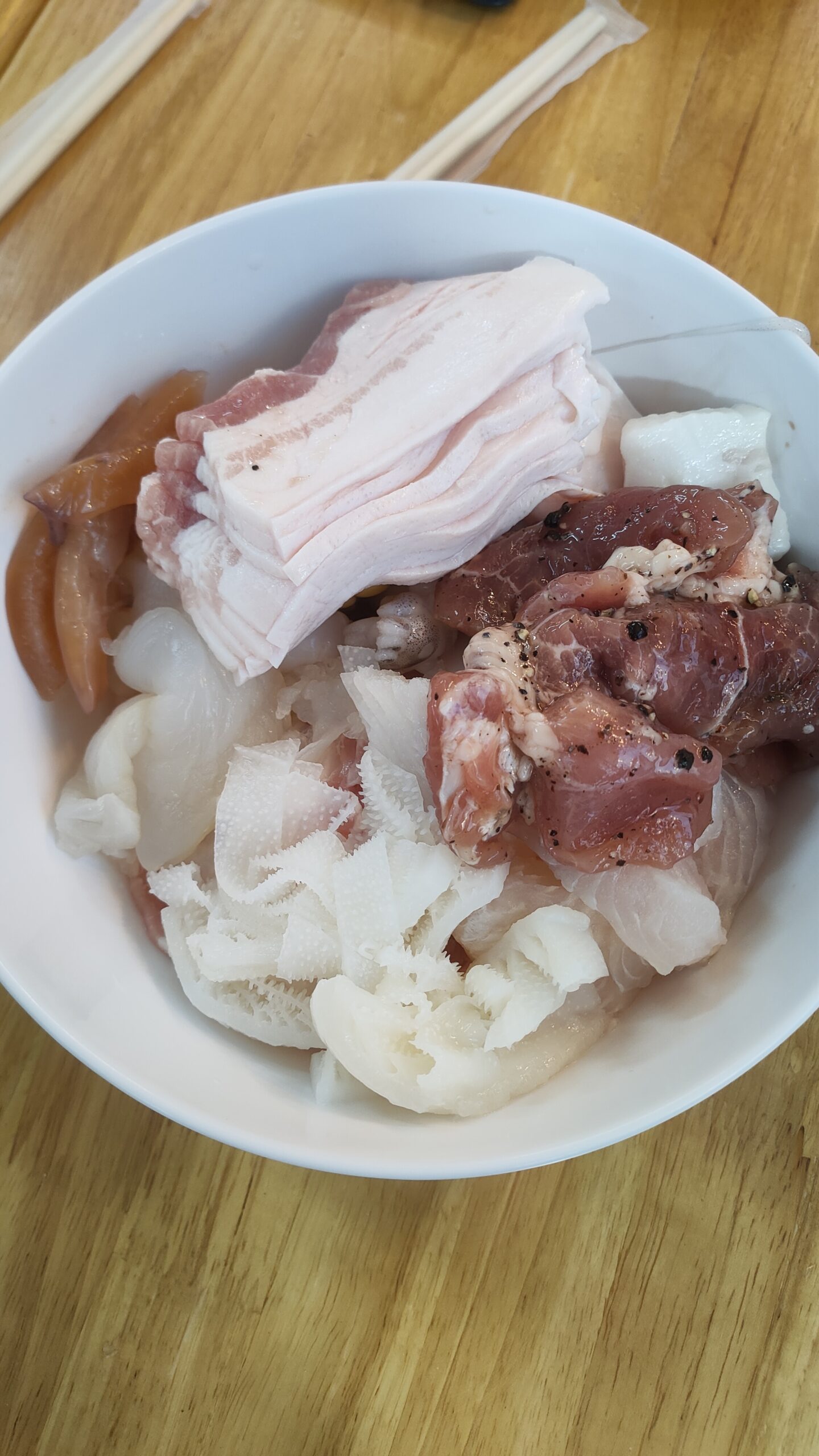 จานเนื้อสดรวมสำหรับปิ้งย่างหรือชาบู มีหมูสามชั้น เนื้อหมักพริกไทย และเครื่องในบนจานขาว