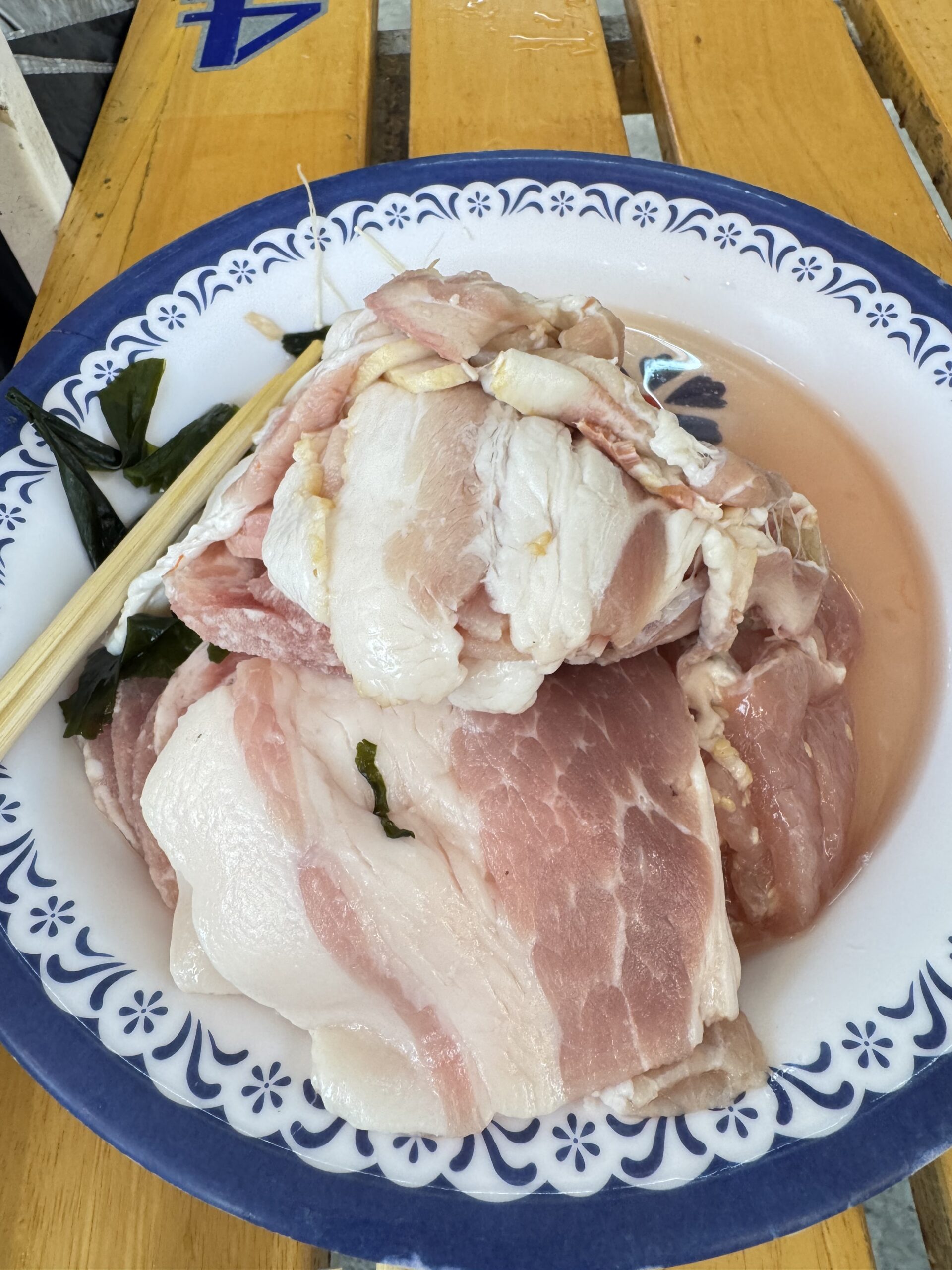 จานหมูสามชั้นดิบและเนื้อหมูหั่นบางพร้อมใบโหระพาและตะเกียบบนจานลายครามสีขาวน้ำเงิน