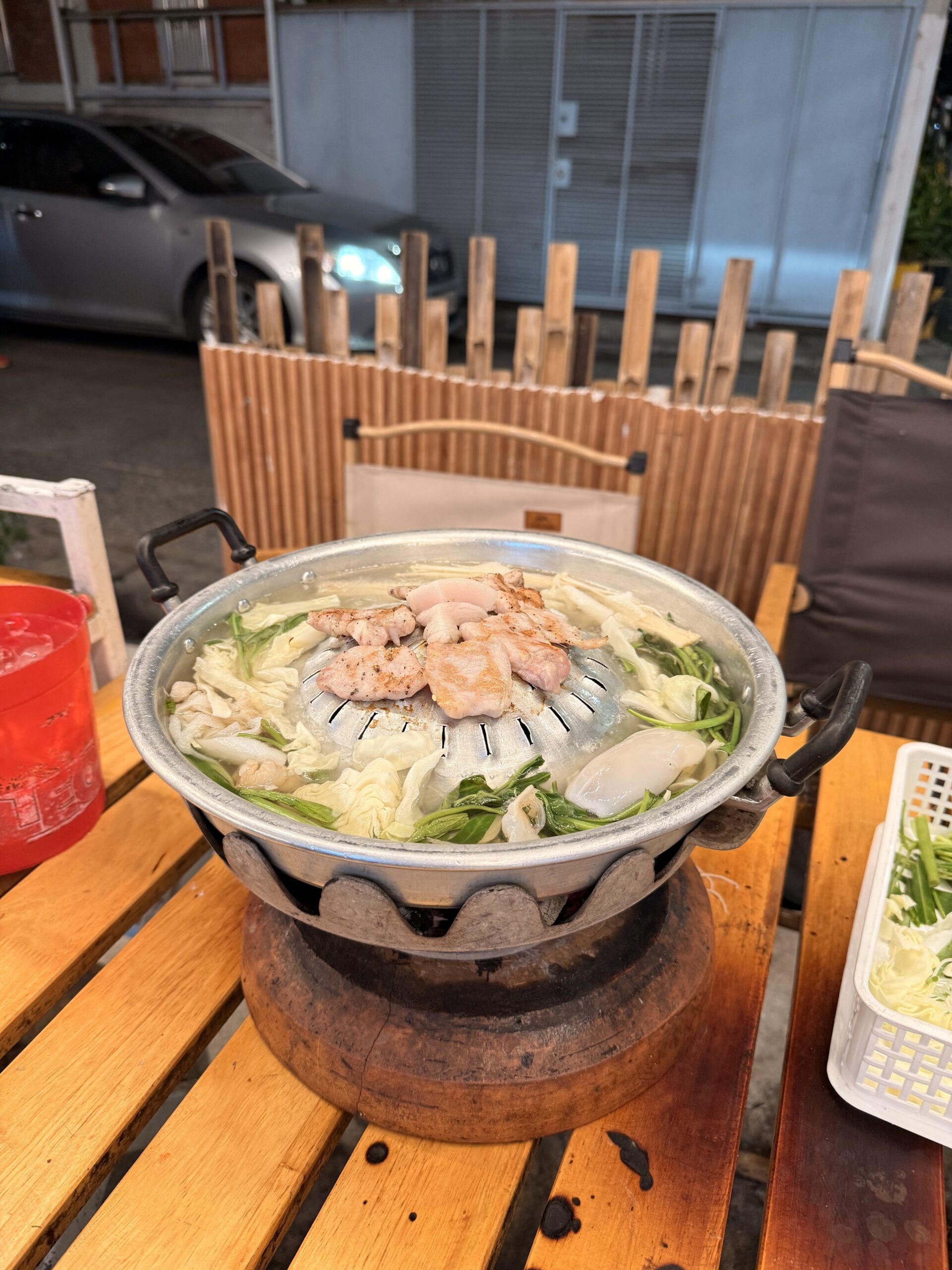 หม้อหมูกระทะบนเตาถ่านพร้อมหมูย่างและผักสดบนโต๊ะไม้หน้าร้านอาหาร