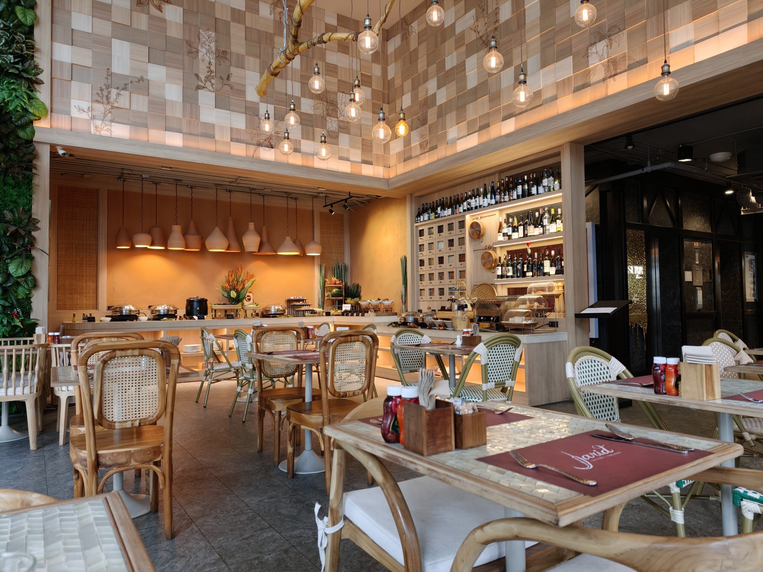 ภายในร้านอาหารตกแต่งด้วยไม้สไตล์โมเดิร์น มีเพดานลายตารางไม้ โคมไฟหลอดเอดิสัน เคาน์เตอร์บุฟเฟ่ต์ ชั้นวางไวน์ และโต๊ะเก้าอี้ไม้หวายจัดเรียงอย่างสวยงาม