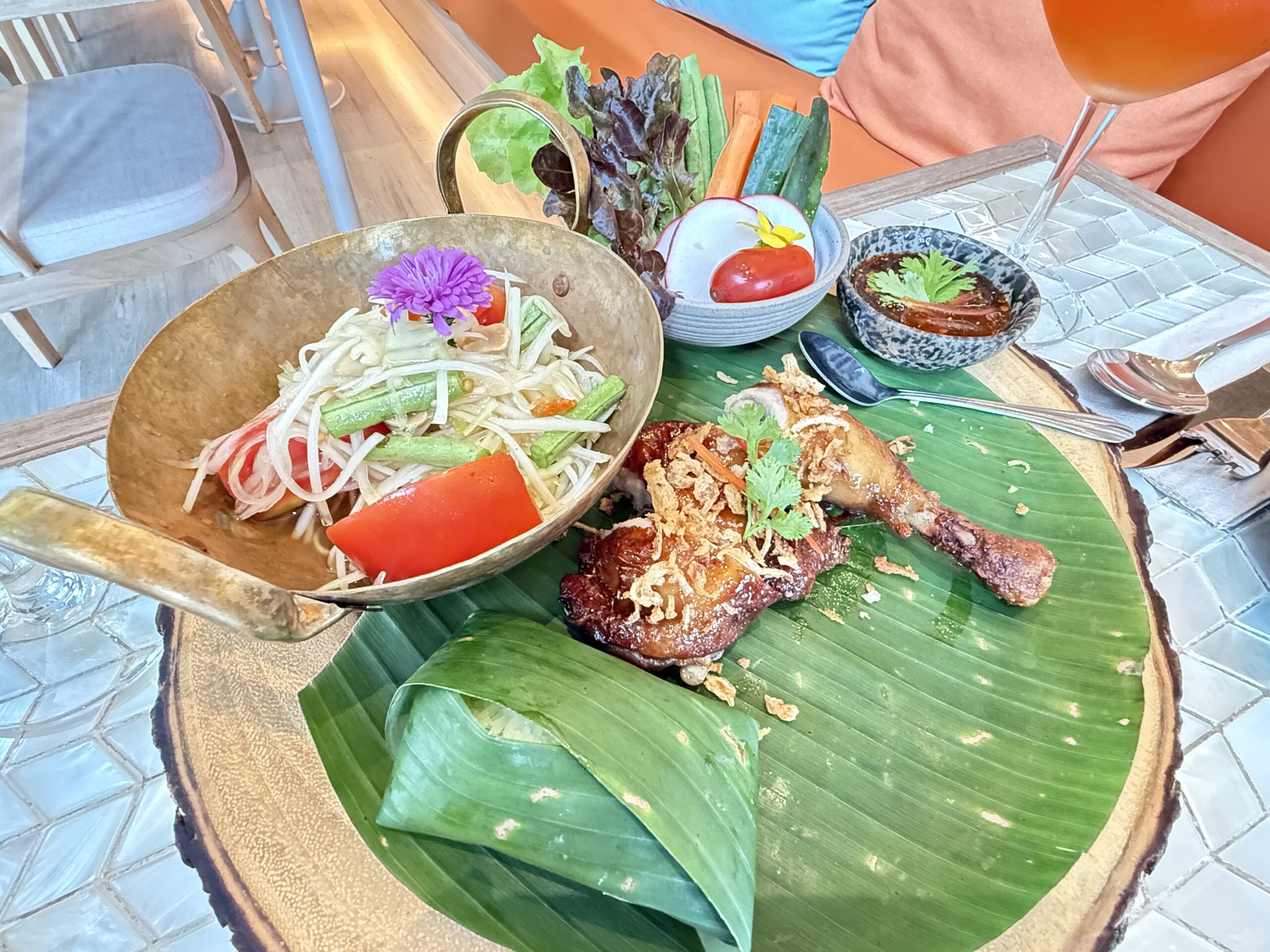 จานส้มตำไทยในกระทะทองเหลืองเสิร์ฟคู่กับไก่ทอดกรอบบนใบตองพร้อมผักสดและน้ำจิ้ม