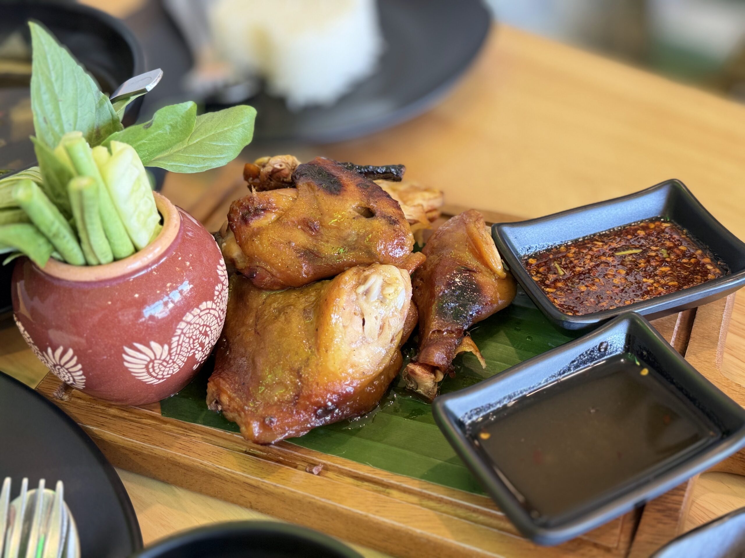 ไก่ย่างเสิร์ฟบนใบตองพร้อมน้ำจิ้มแจ่วและผักสดในถ้วยดินเผา