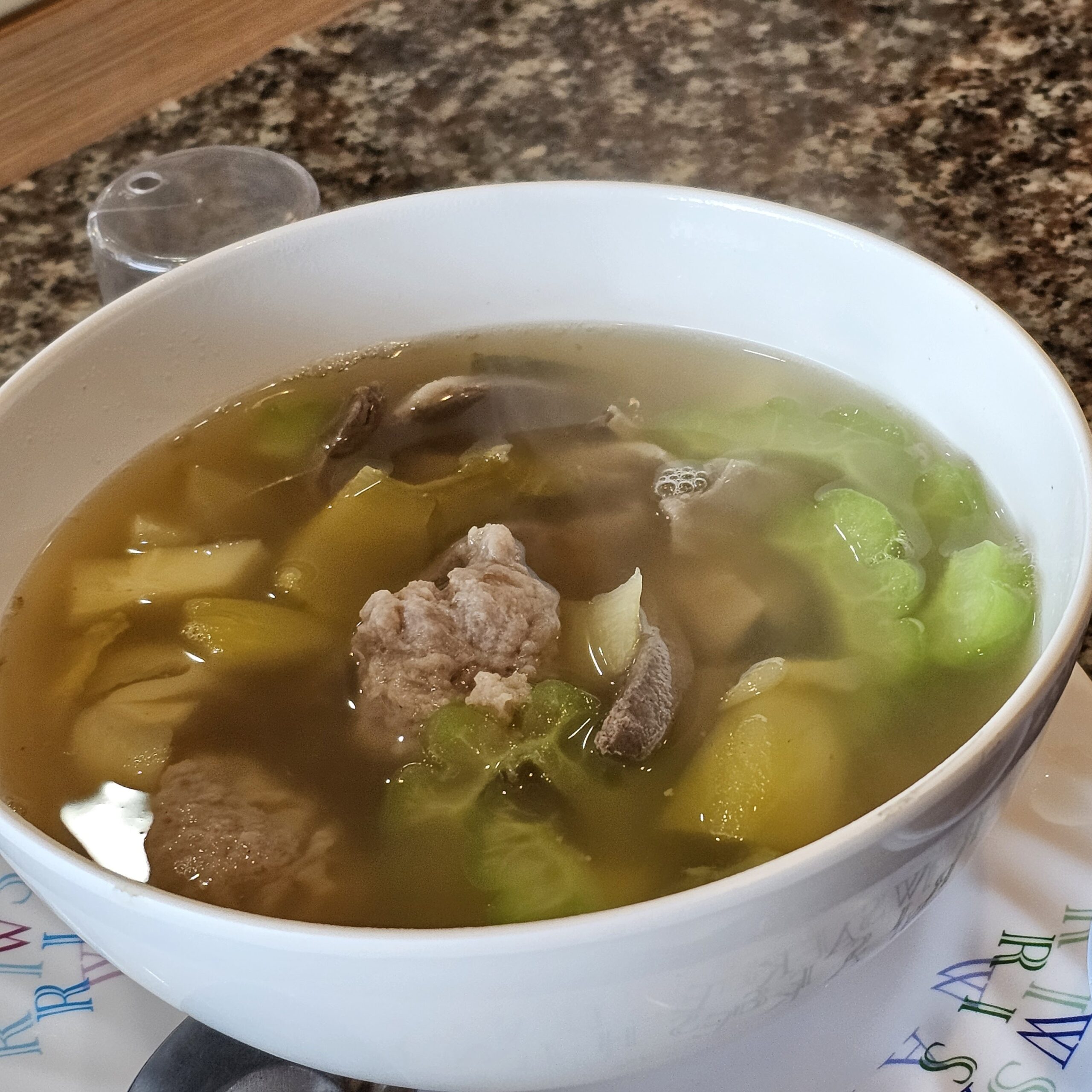 ชามซุปใสใส่ลูกชิ้นหมูสับ เห็ดหอม และผักกาดเขียว เสิร์ฟในชามสีขาว