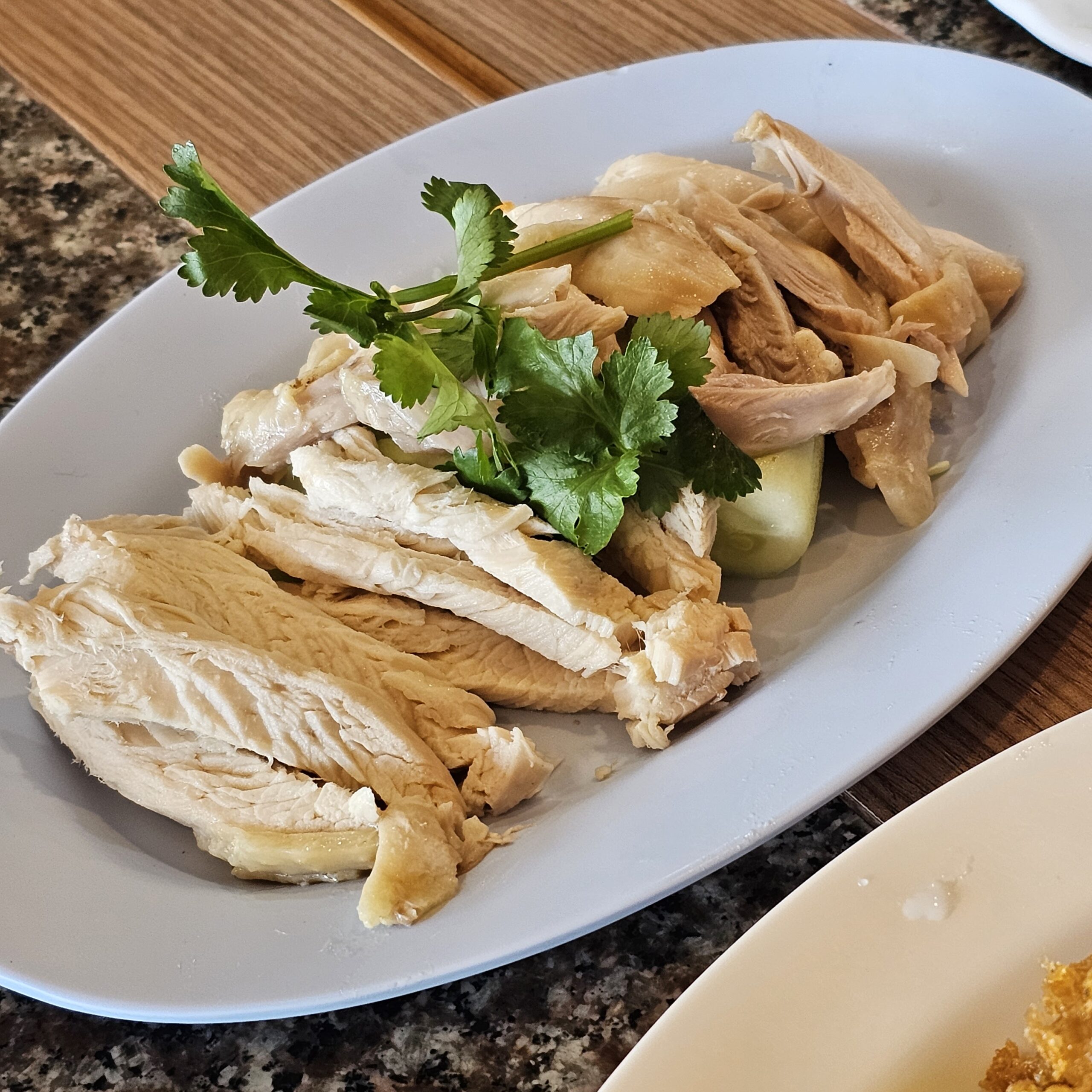 ข้าวมันไก่ เนื้อไก่ต้มหั่นชิ้นเรียงบนจานขาว ตกแต่งด้วยผักชีและแตงกวา