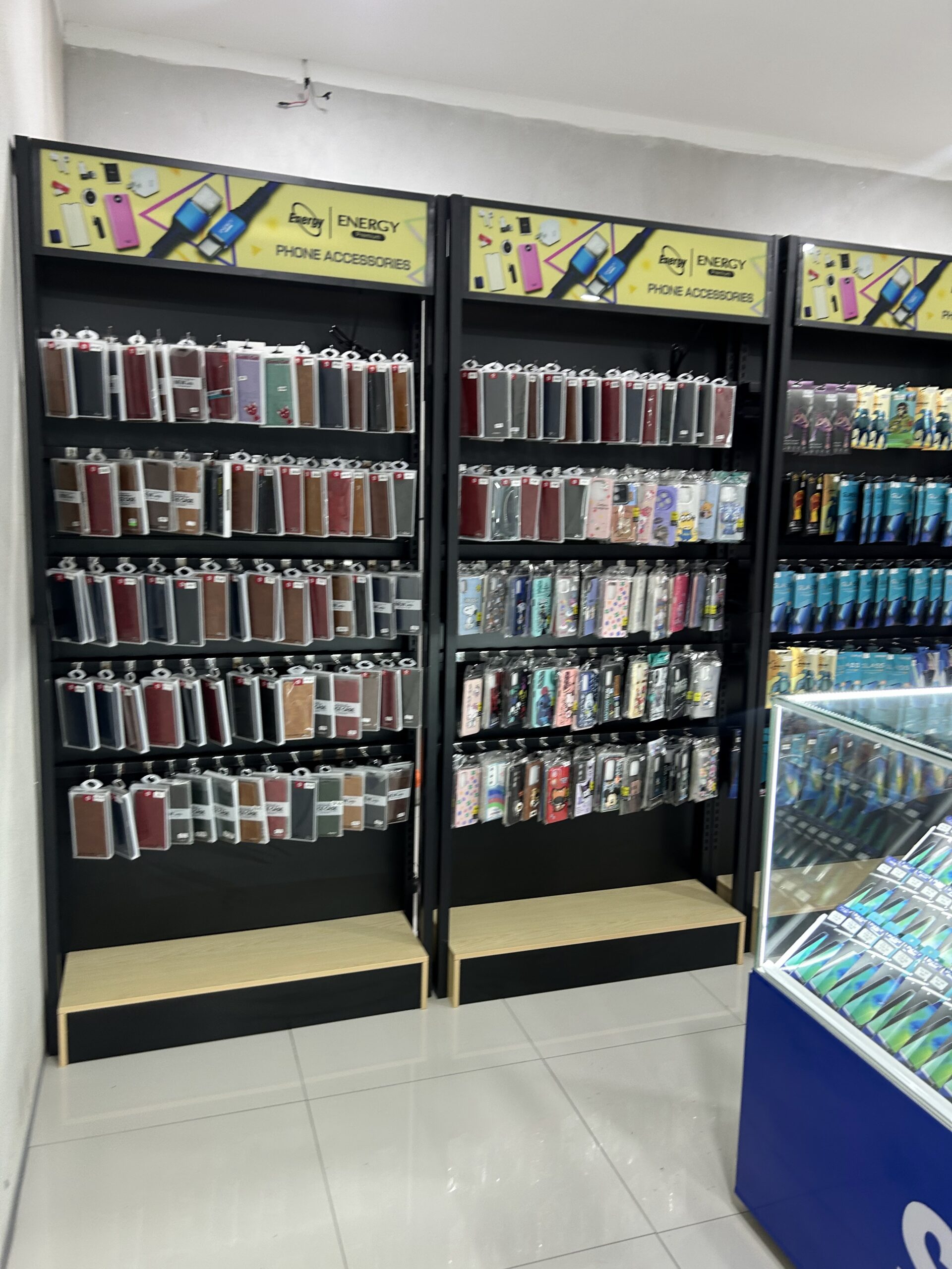 ชั้นวางอุปกรณ์เสริมโทรศัพท์มือถือแบรนด์ Energy เคสโทรศัพท์หลากสีหลายรุ่นเรียงบนชั้นสีดำในร้าน