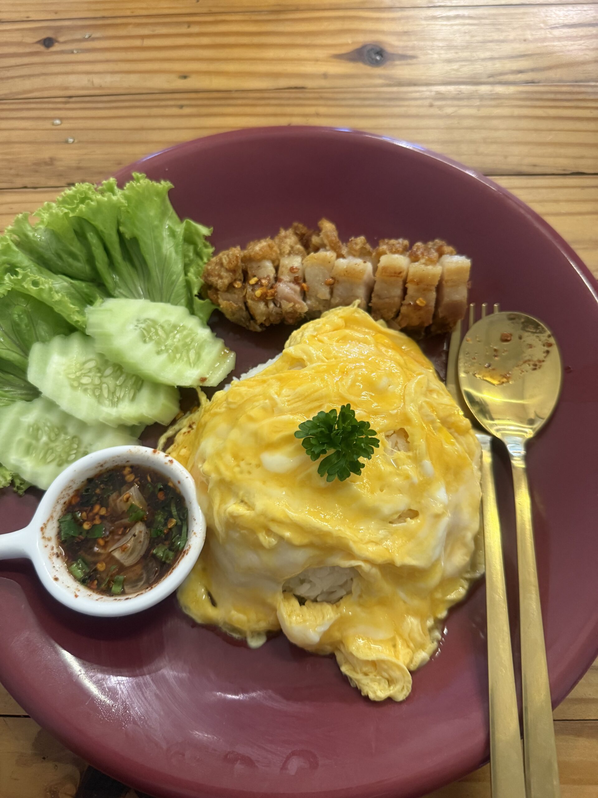 ข้ามไข่เจียวห่อราดหน้าพร้อมหมูกรอบหั่นชิ้น เสิร์ฟกับแตงกวา ผักกาดหอม และน้ำจิ้มแจ่วบนจานสีม่วง