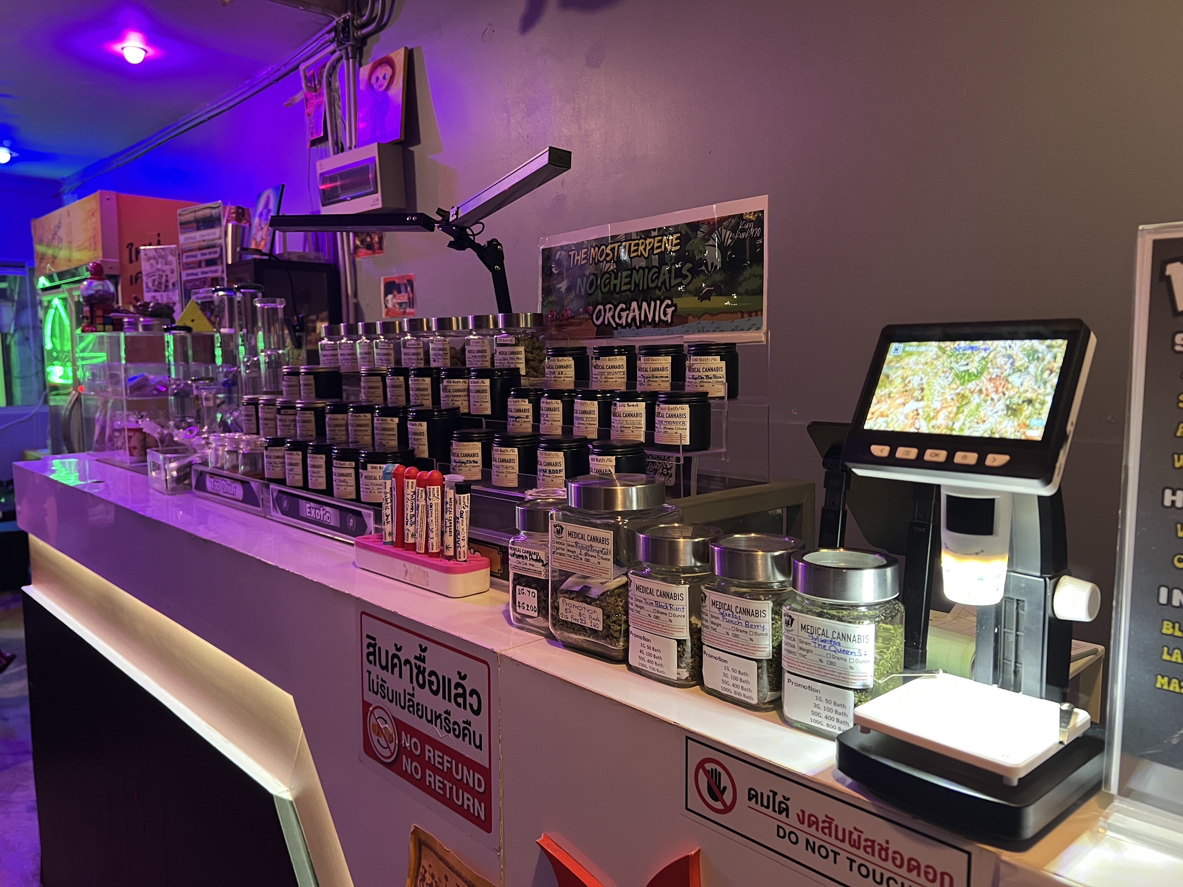 เคาน์เตอร์ร้านขายกัญชาทางการแพทย์ในประเทศไทย มีขวดโหลกัญชาเรียงรายบนชั้นวาง พร้อมเครื่องชั่งดิจิทัลและป้ายไม่รับคืนสินค้า