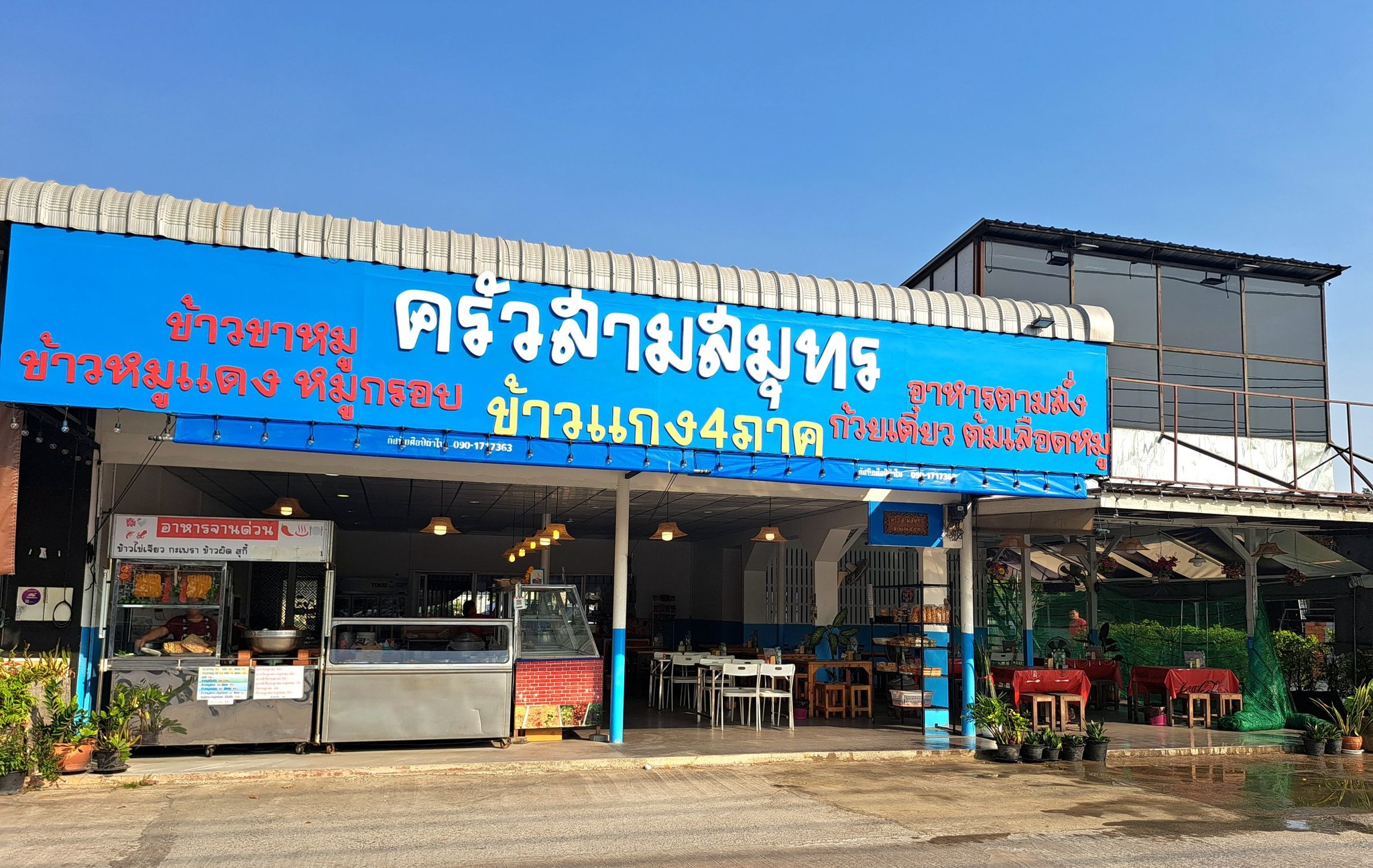 ร้านครัวสามสมุทร ร้านอาหารไทยพร้อมป้ายสีฟ้าขนาดใหญ่ มีข้าวแกง 4 ภาค ข้าวขาหมู ข้าวหมูแดง หมูกรอบ ก๋วยเตี๋ยว และต้มเลือดหมู