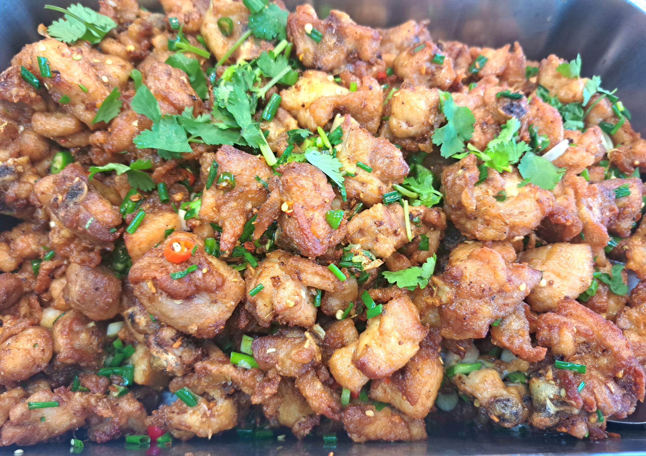 ไก่ทอดเกลือพริกโรยผักชีและต้นหอมซอย เสิร์ฟบนจานดำ