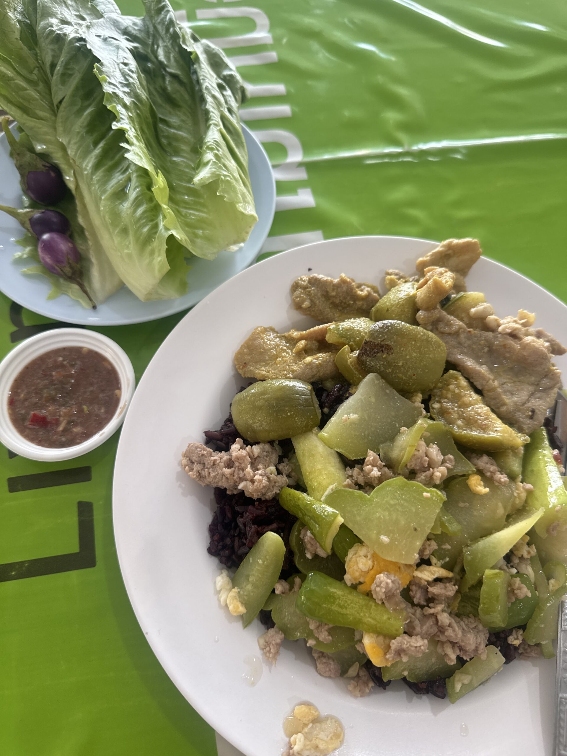 จานข้าวไรซ์เบอร์รี่ราดผัดมะเขือยาวกับหมูสับและไข่ พร้อมผักสดและน้ำพริกกะปิ บนโต๊ะสีเขียว