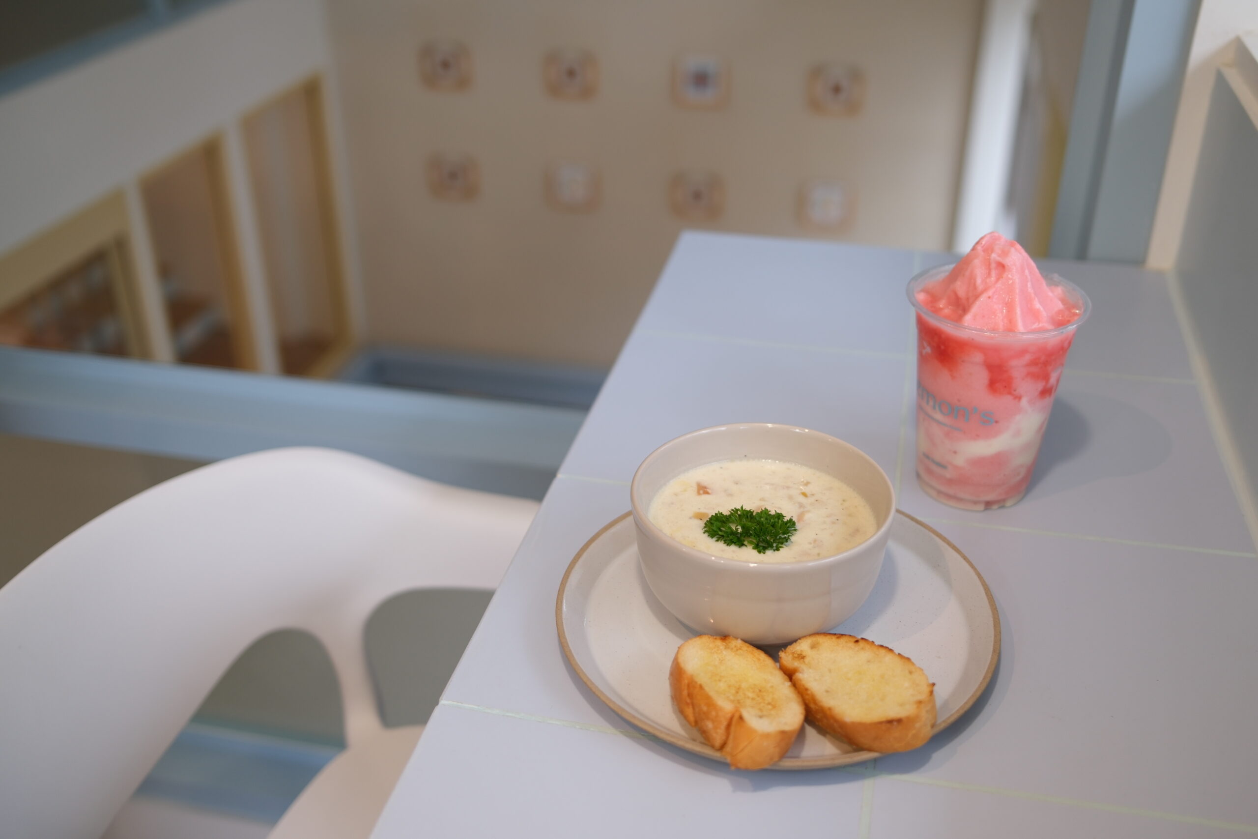 ซุปครีมในชามพร้อมขนมปังกรอบบนจานและเครื่องดื่มสมูทตี้สีชมพูในร้านคาเฟ่สไตล์น่ารัก