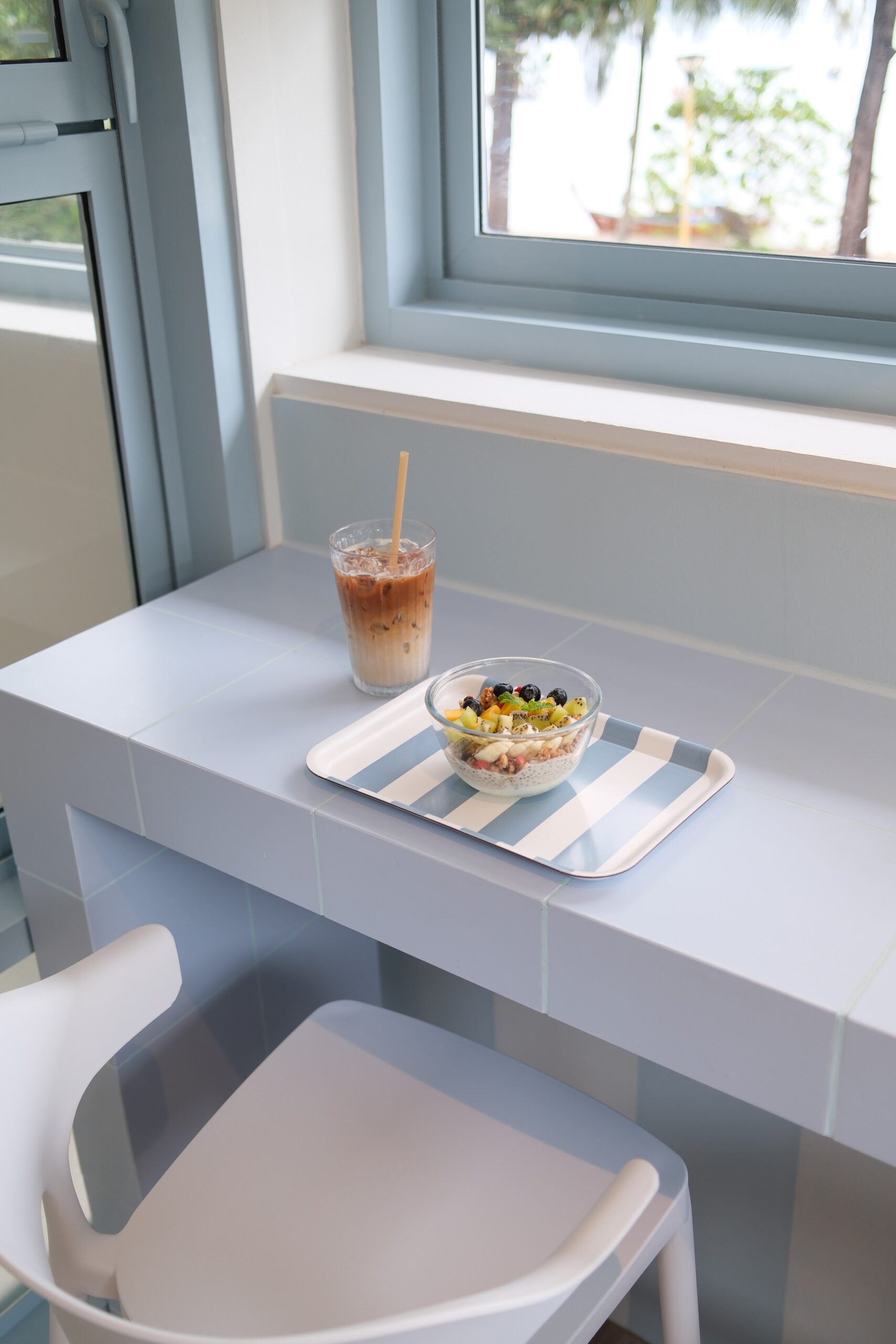 กาแฟเย็นและชามอาซาอีโบวล์กับผลไม้สดบนเคาน์เตอร์กระเบื้องสีฟ้าพาสเทลในคาเฟ่สไตล์มินิมอล