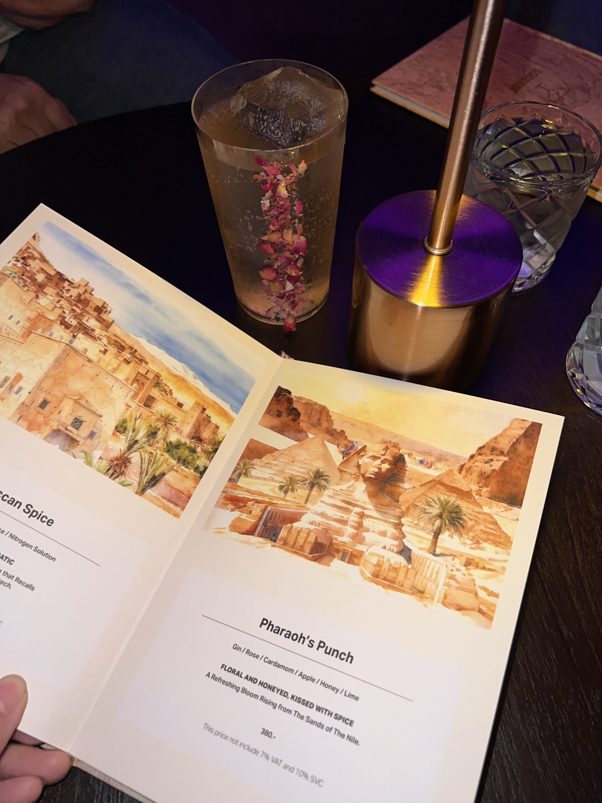 เมนูค็อกเทล Pharaoh's Punch พร้อมเครื่องดื่มตกแต่งด้วยกลีบกุหลาบในแก้วใส ราคา 380 บาท ส่วนผสมจิน กุหลาบ กระวาน แอปเปิ้ล น้ำผึ้ง และมะนาว