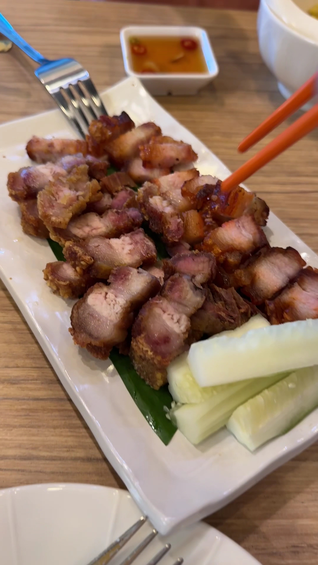 หมูกรอบทอดหั่นชิ้นเสิร์ฟบนจานสี่เหลี่ยมพร้อมแตงกวาและน้ำจิ้มพริก