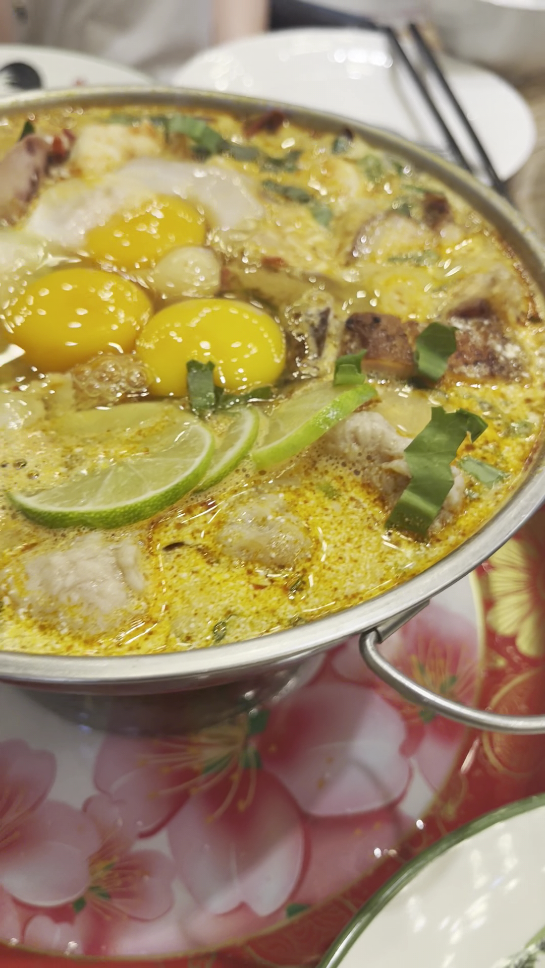 หม้อไฟอาหารทะเลในน้ำซุปสีเหลืองกับไข่แดง มะนาว และผักชี เสิร์ฟในหม้อสแตนเลสบนโต๊ะอาหาร