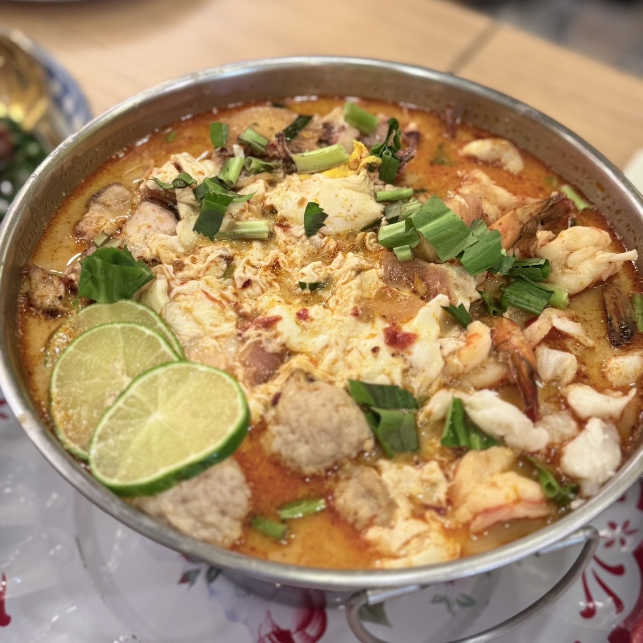 ต้มยำทะเลรวมมิตรในหม้อสแตนเลส มีกุ้ง ลูกชิ้น ไข่ และมะนาวฝานเป็นแว่น โรยต้นหอมซอย