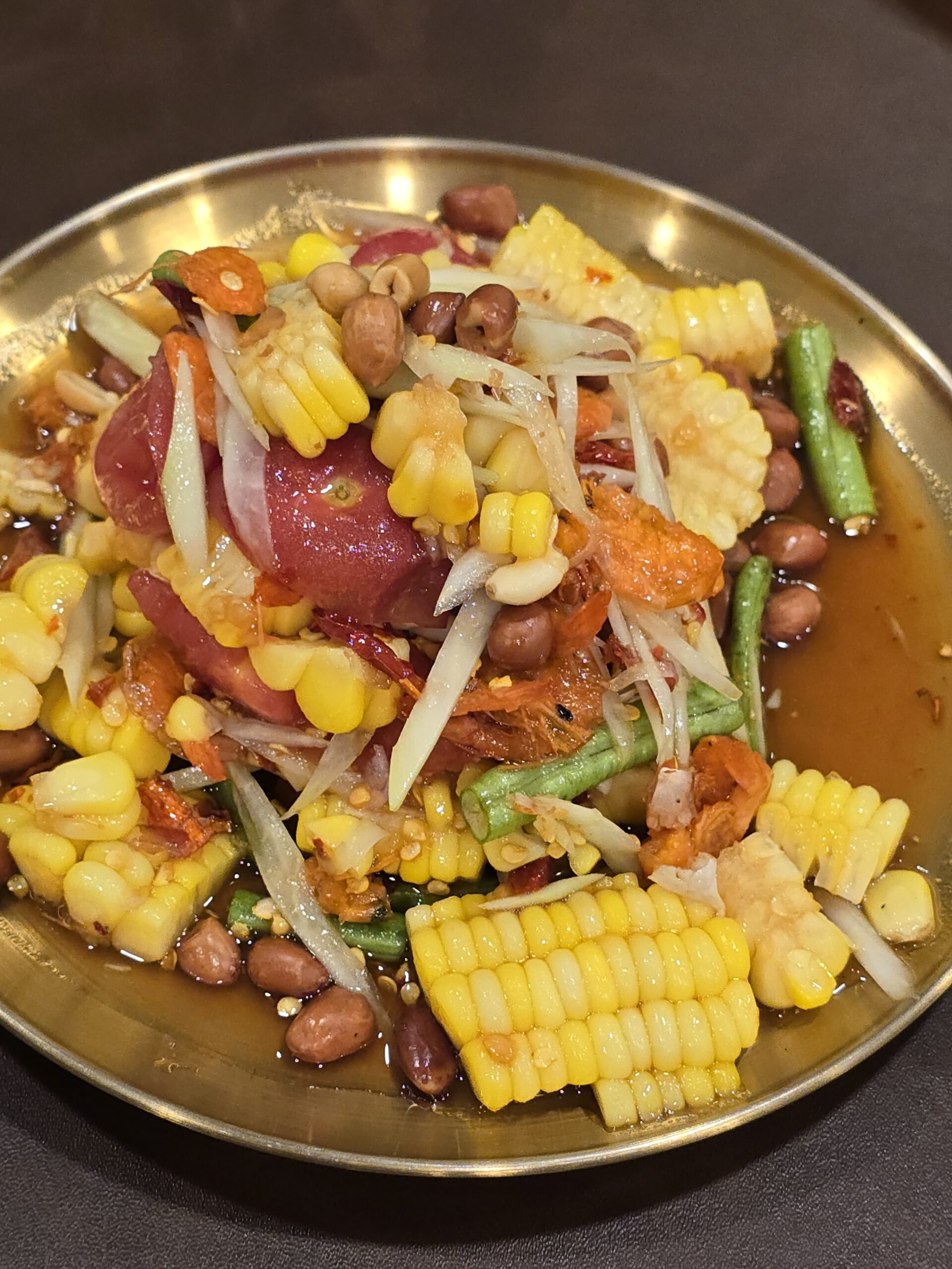 ส้มตำข้าวโพดใส่ถั่วลิสง แครอท ถั่วฝักยาว และกุ้งแห้ง เสิร์ฟในจานทองเหลือง