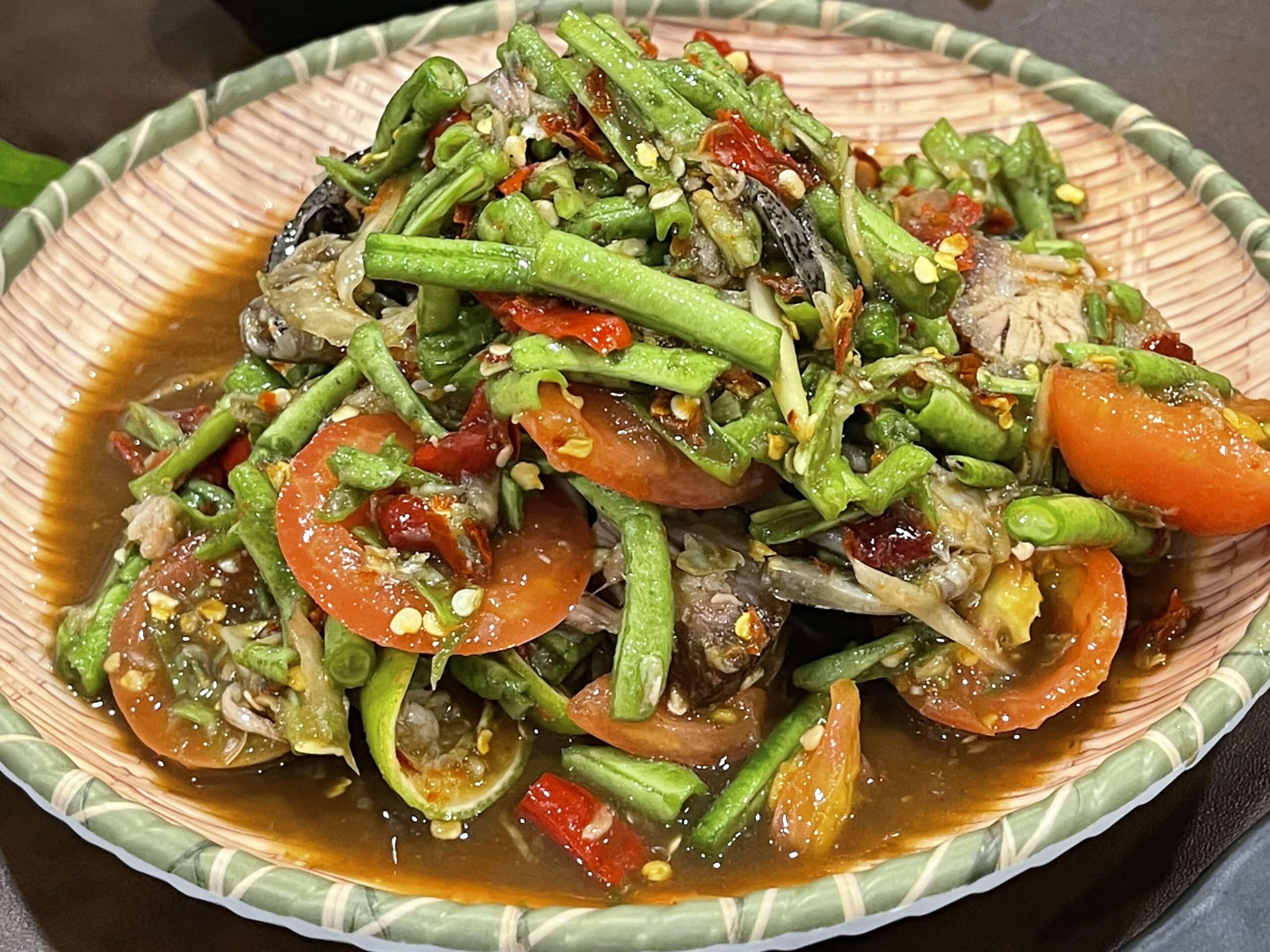 ส้มตำถั่วฝักยาวใส่มะเขือเทศ พริกแห้ง และปลาร้า จัดเสิร์ฟบนจานสานไม้ไผ่