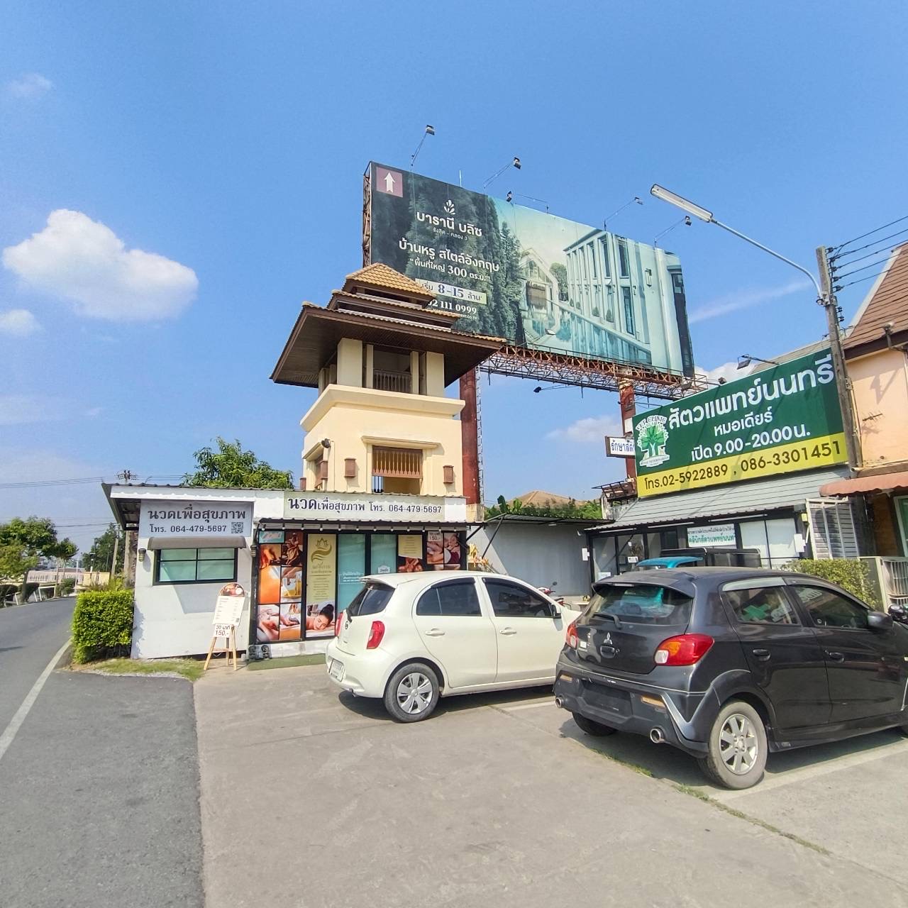 ร้านนวดเพื่อสุขภาพและคลินิกสัตวแพทย์นนทรีริมถนน มีป้ายโฆษณาขนาดใหญ่และรถจอดหน้าร้าน