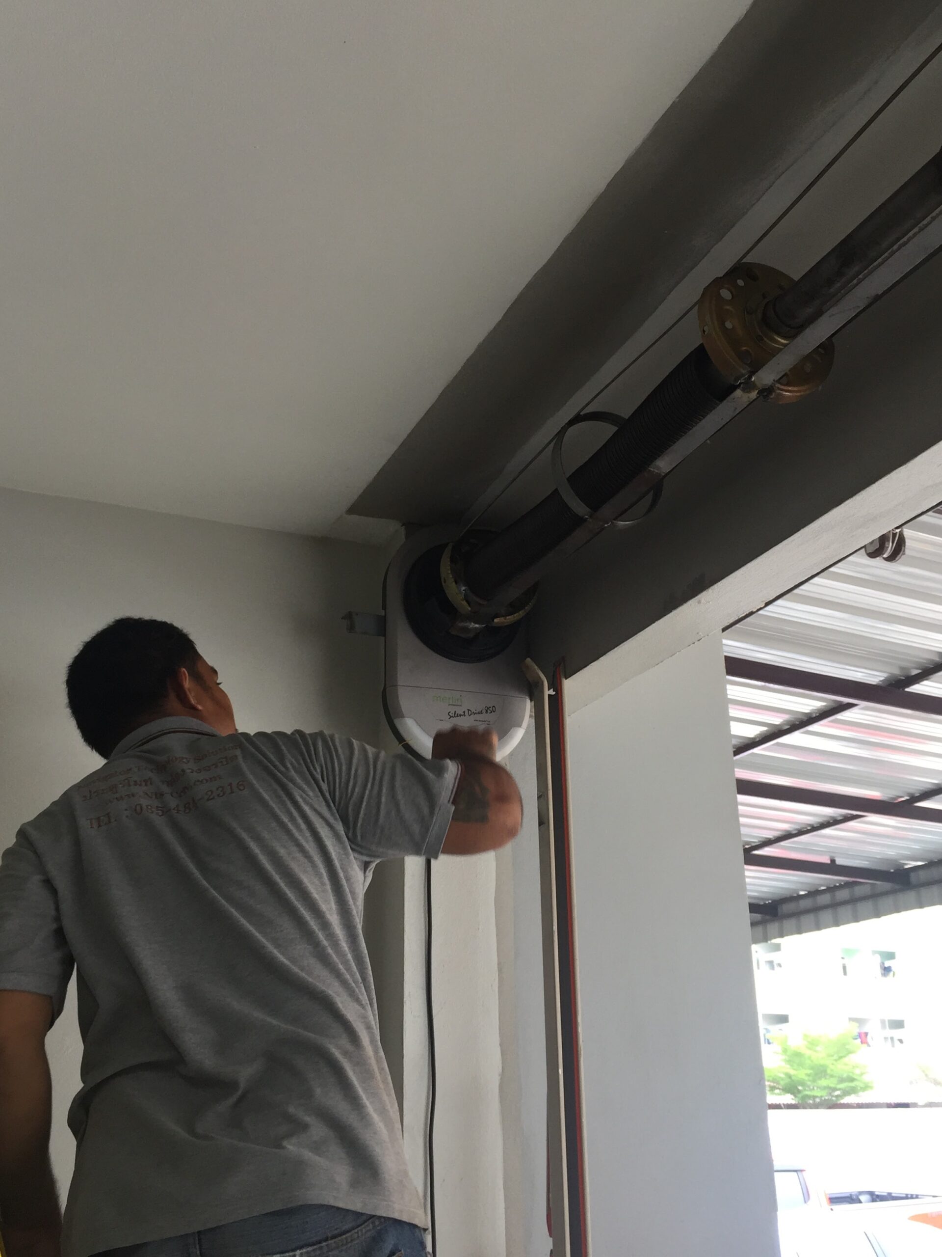 ช่างกำลังติดตั้งมอเตอร์ประตูม้วนไฟฟ้าที่ด้านบนของประตู