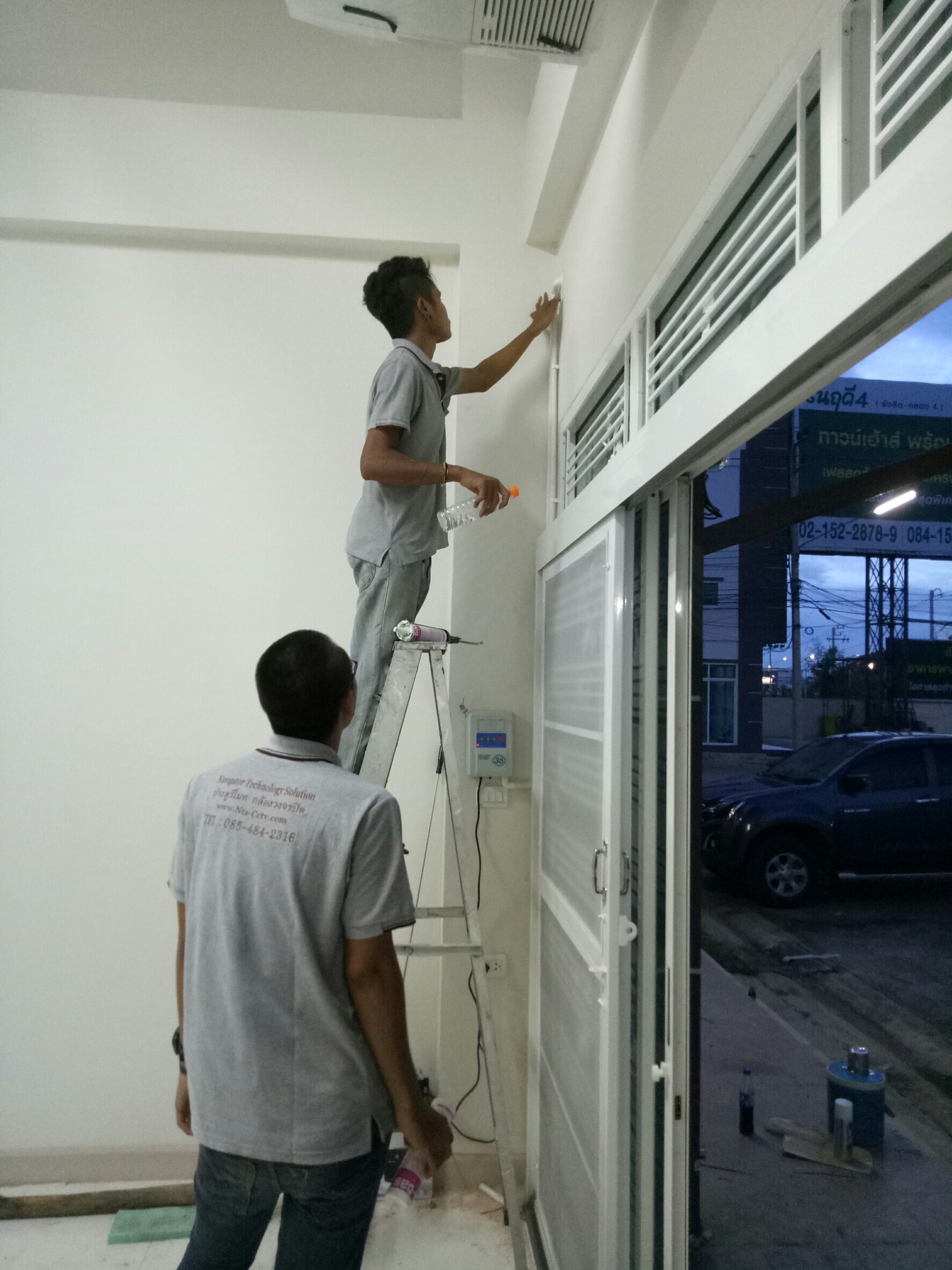 ช่างเทคนิคสองคนกำลังติดตั้งอุปกรณ์บริเวณหน้าร้านโดยใช้บันไดพับ