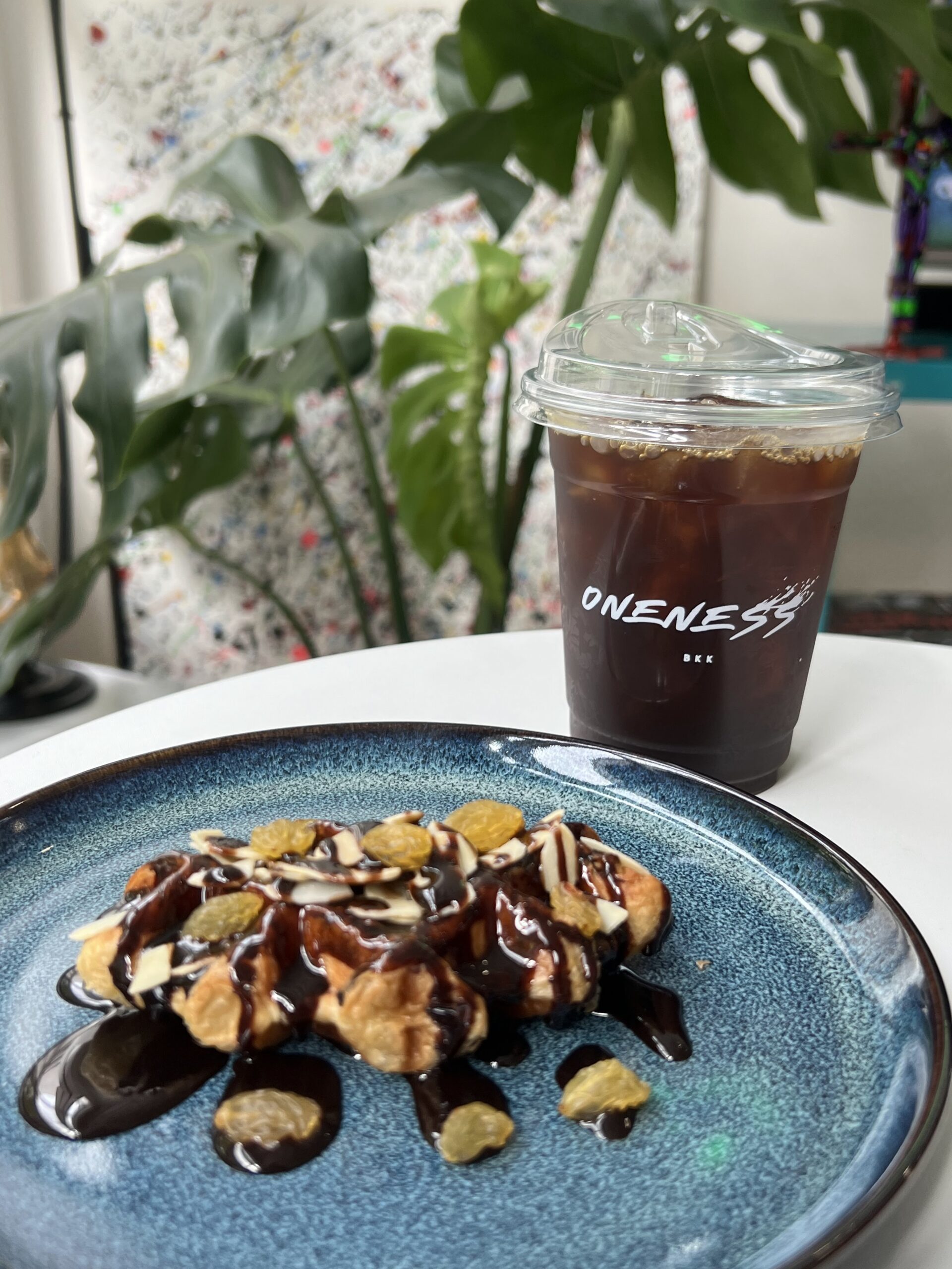 วาฟเฟิลราดซอสช็อกโกแลตและไวท์ช็อกโกแลตพร้อมกาแฟเย็นในแก้ว Oneness BKK บนจานสีน้ำเงินเข้ม