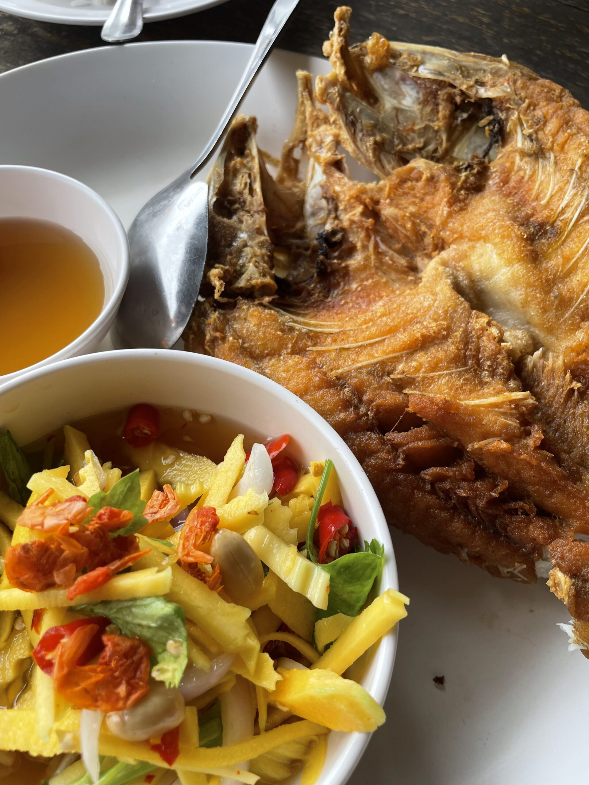 ปลาทอดกรอบทั้งตัวเสิร์ฟพร้อมยำมะม่วงสดและน้ำจิ้มในชามขาว