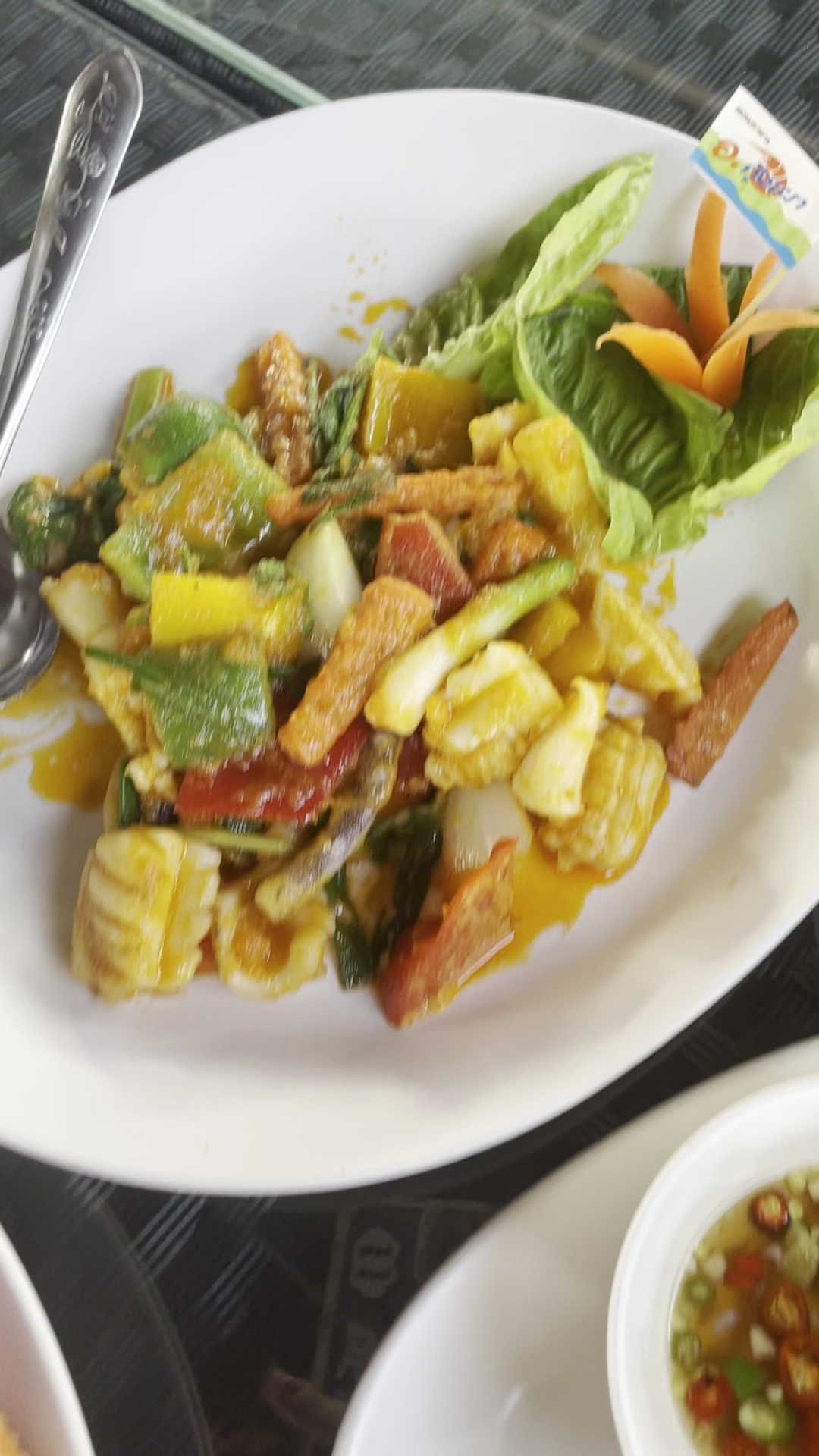 จานผัดผักรวมกับซีฟู้ดและไข่ในซอสเหลืองเสิร์ฟพร้อมผักสดแกะสลักบนจานขาว