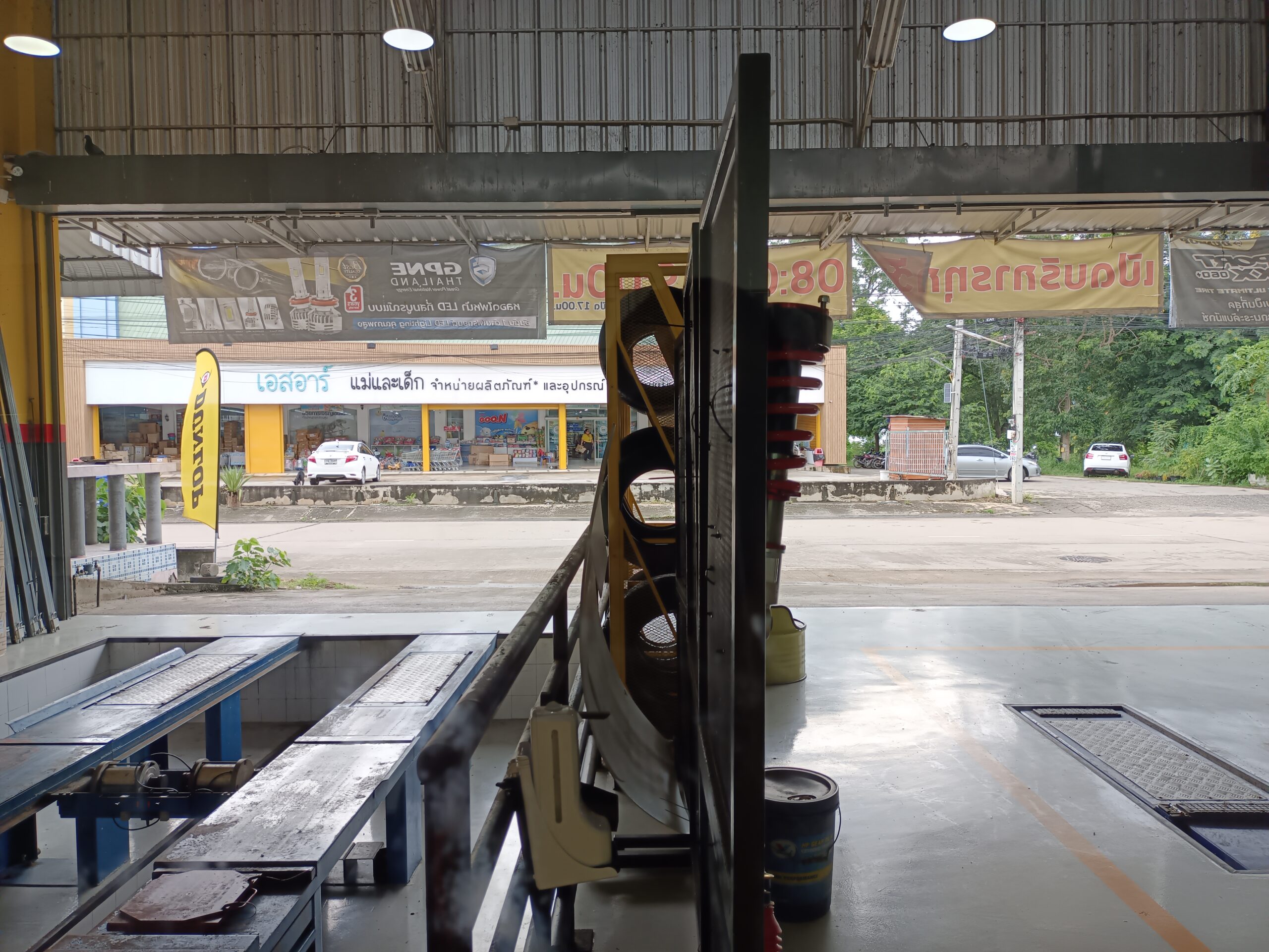อู่ซ่อมรถในประเทศไทย มีลิฟต์ยกรถและอุปกรณ์ซ่อม มองออกไปเห็นร้านค้าฝั่งตรงข้ามถนน