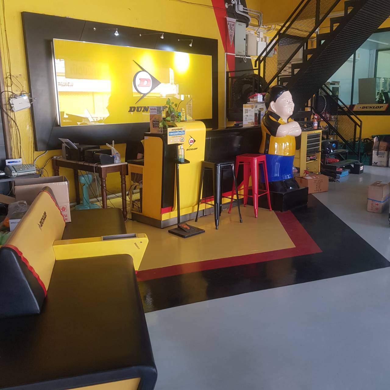 พื้นที่รับรองลูกค้าร้านยางรถยนต์ Dunlop ตกแต่งสีเหลืองดำ มีโซฟา เคาน์เตอร์ และตุ๊กตาประดับ