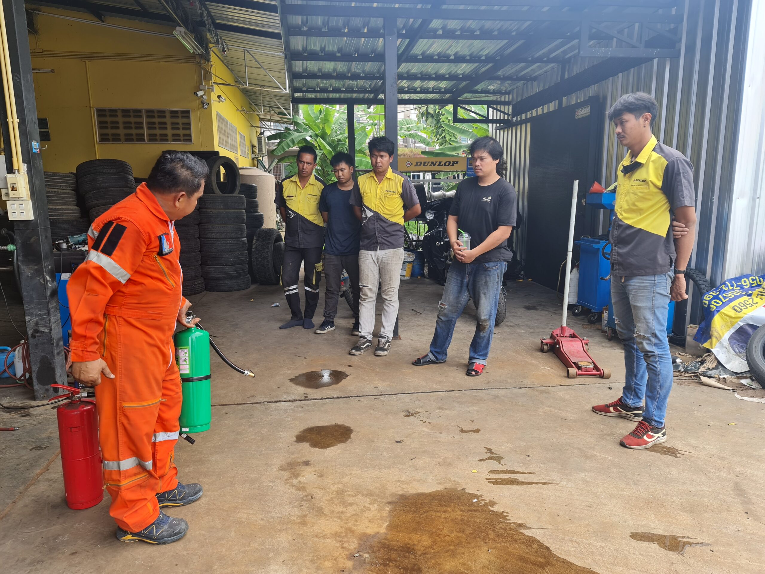 การฝึกอบรมดับเพลิงในร้านยางรถยนต์ โดยเจ้าหน้าที่ในชุดสีส้มสาธิตการใช้ถังดับเพลิงให้พนักงานดู
