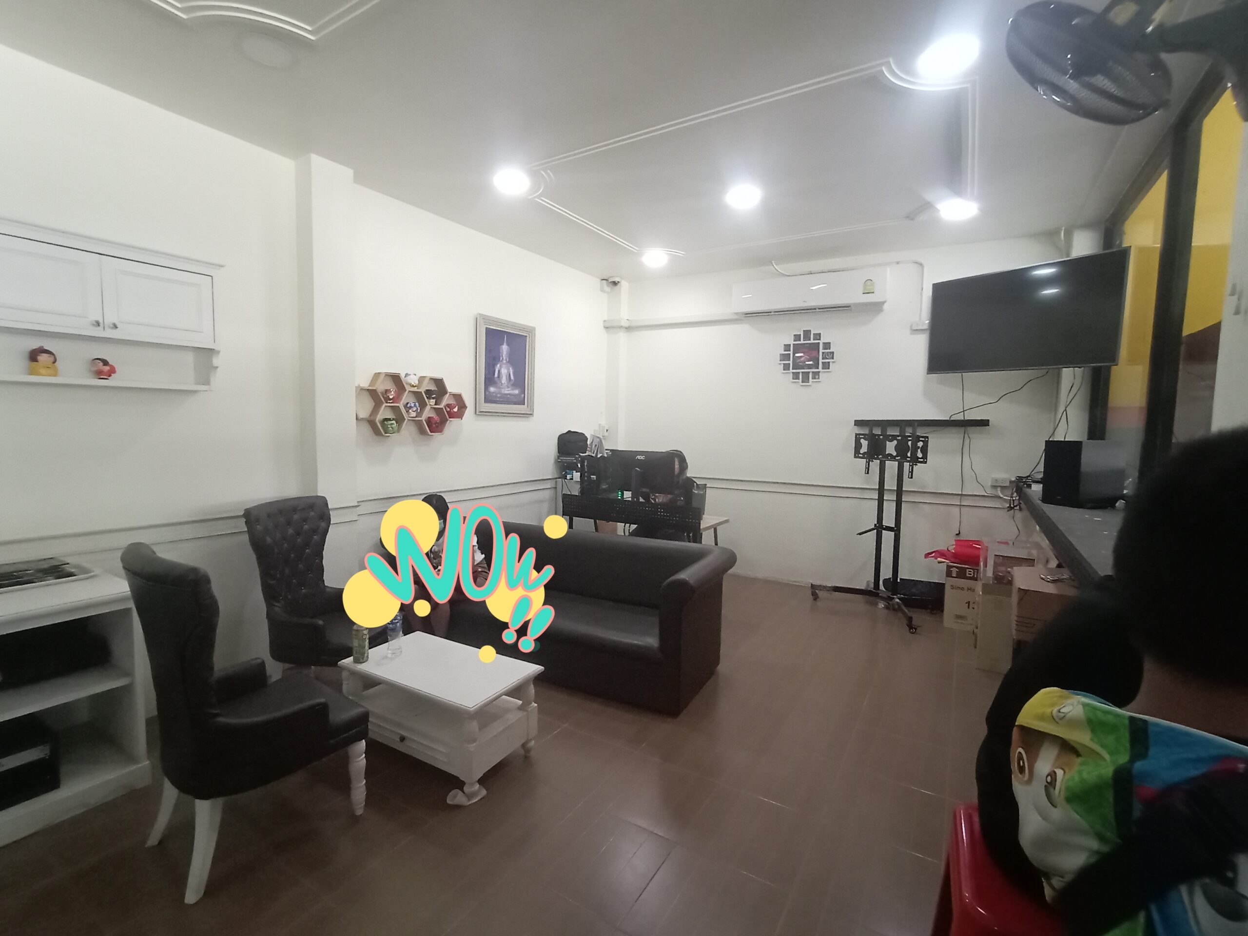 ห้องนั่งเล่นภายในร้านอาหารพร้อมโซฟาสีดำ เก้าอี้หนัง โต๊ะกลางสีขาว ทีวีจอแบน และแอร์ ตกแต่งสไตล์โมเดิร์น