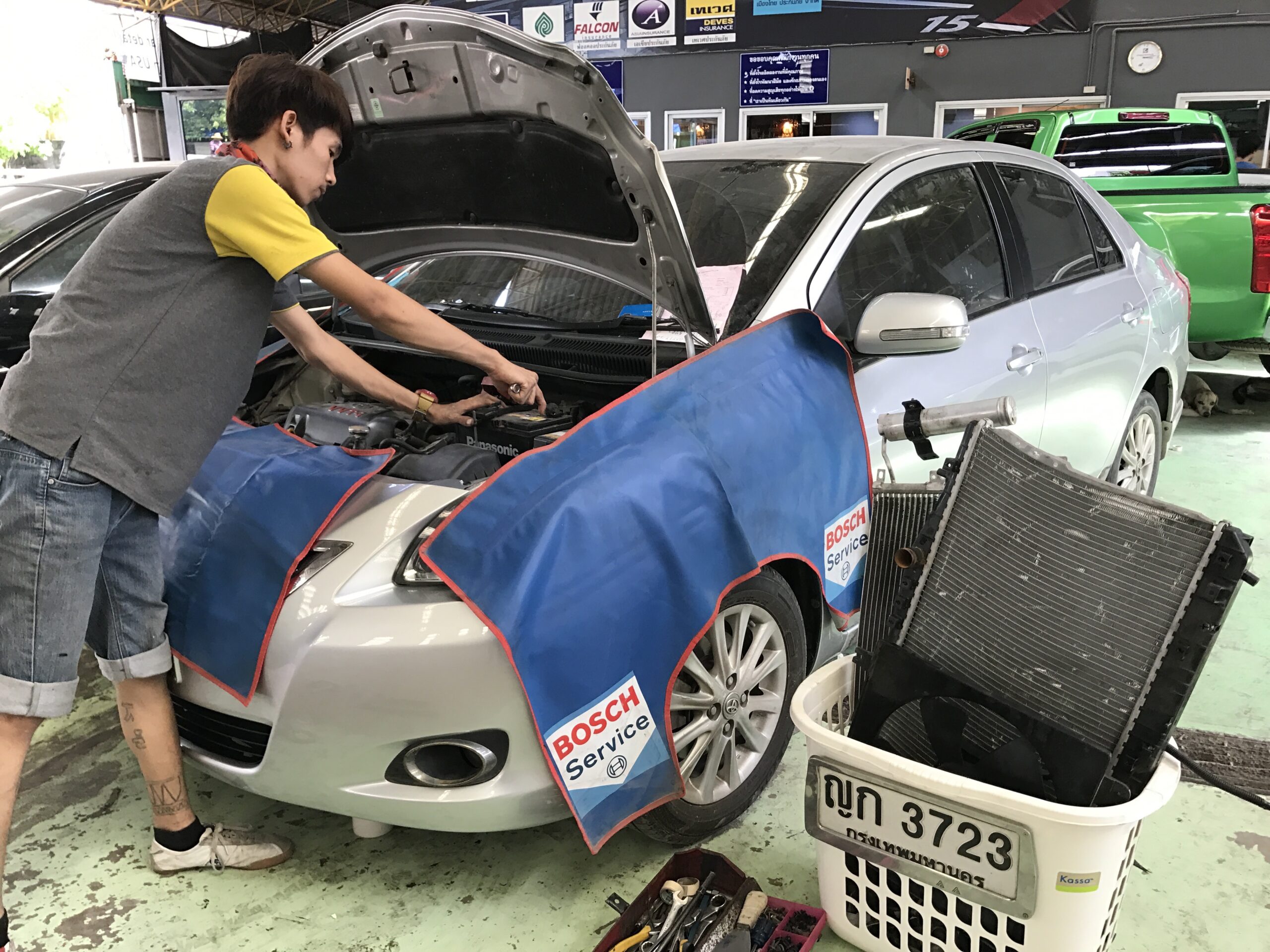 ช่างซ่อมรถยนต์กำลังซ่อมเครื่องยนต์ที่ศูนย์บริการ Bosch Service พร้อมผ้าคลุมป้องกันสีรถ